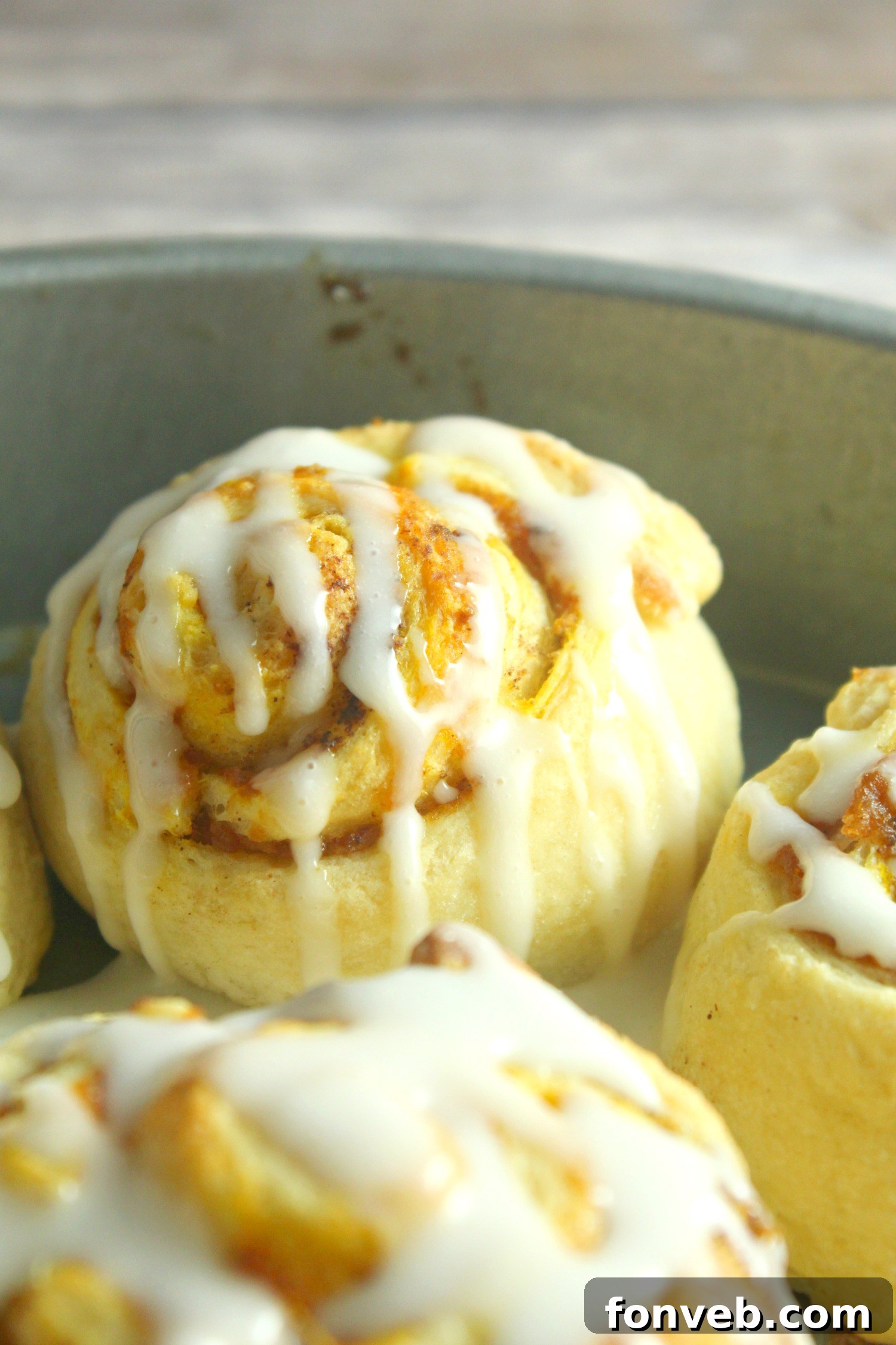 A serving of two pumpkin cinnamon rolls on a plate, showing the soft, moist interior and ample frosting.