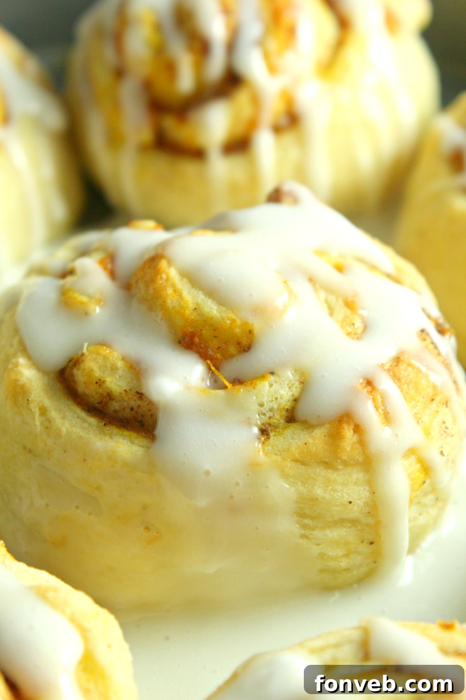 Artistic shot of frosted pumpkin cinnamon rolls in a rustic setting, emphasizing autumnal coziness.