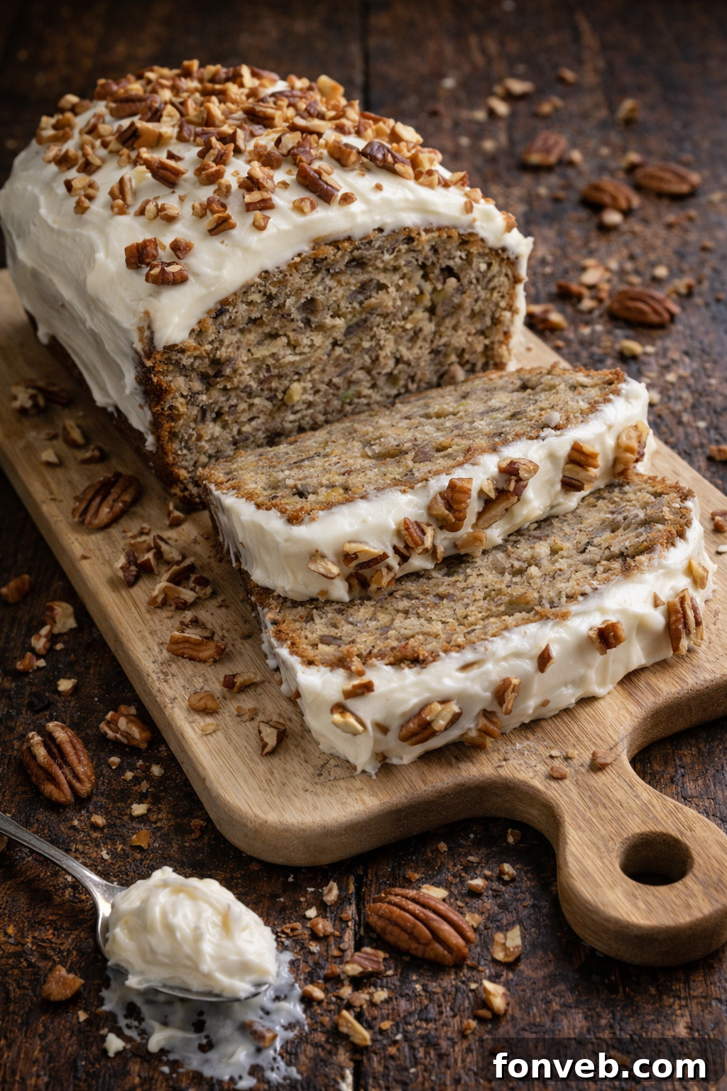 Two slices of Southern Hummingbird Bread on a white plate, showcasing its moist crumb, fruit, nuts, and thick cream cheese frosting. A whole loaf is visible in the background.