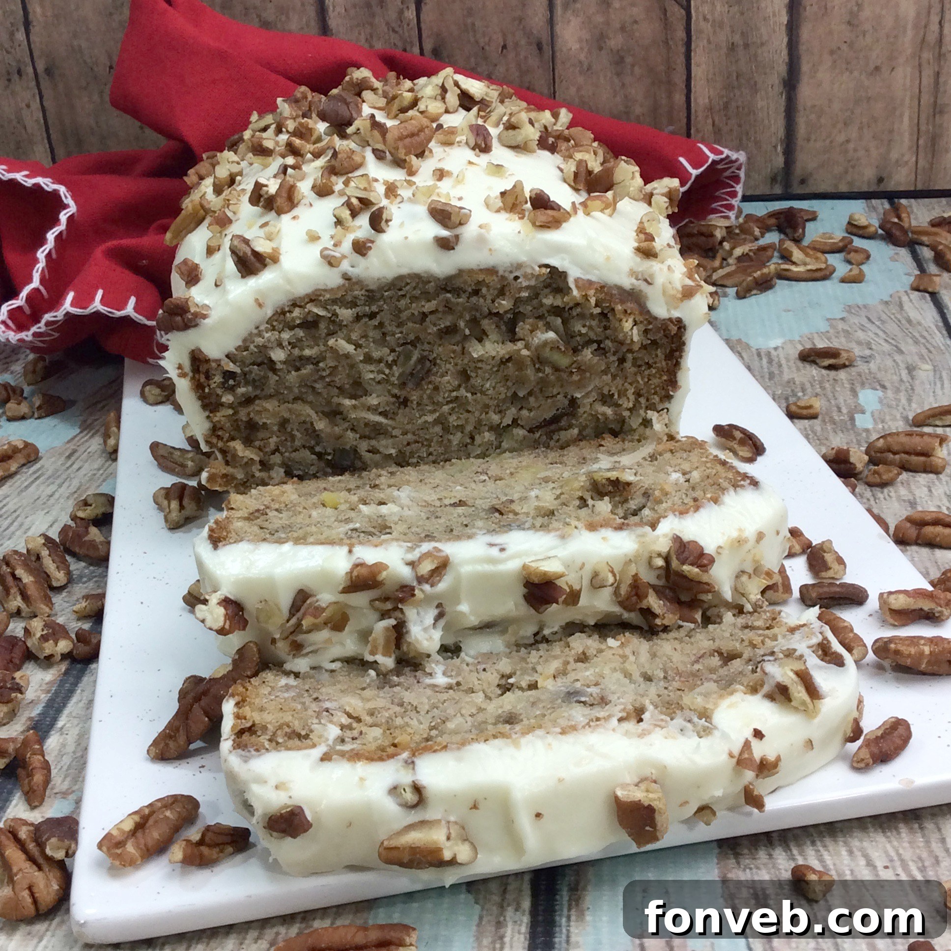 A close-up of a frosted slice of Southern Hummingbird Bread, topped with additional chopped pecans, invitingly presented.