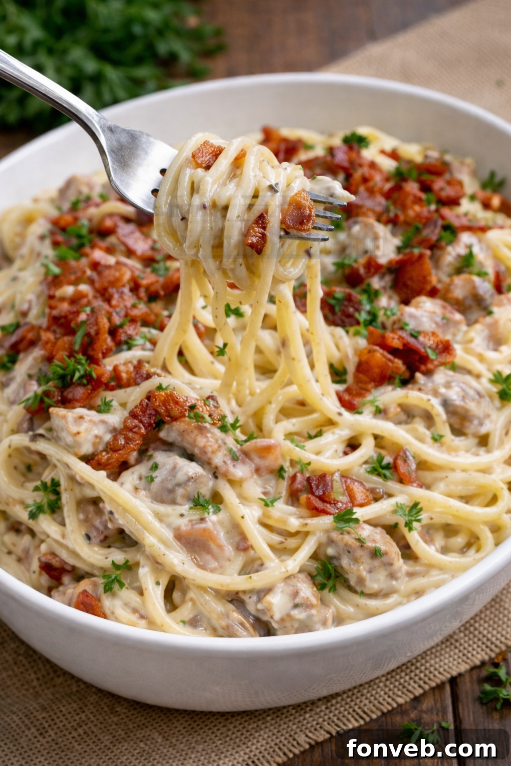 A close-up shot of Creamy Bacon Carbonara with Chicken in a white bowl, with a fork lifting a generous bite of pasta, showcasing the creamy sauce and crisp bacon.