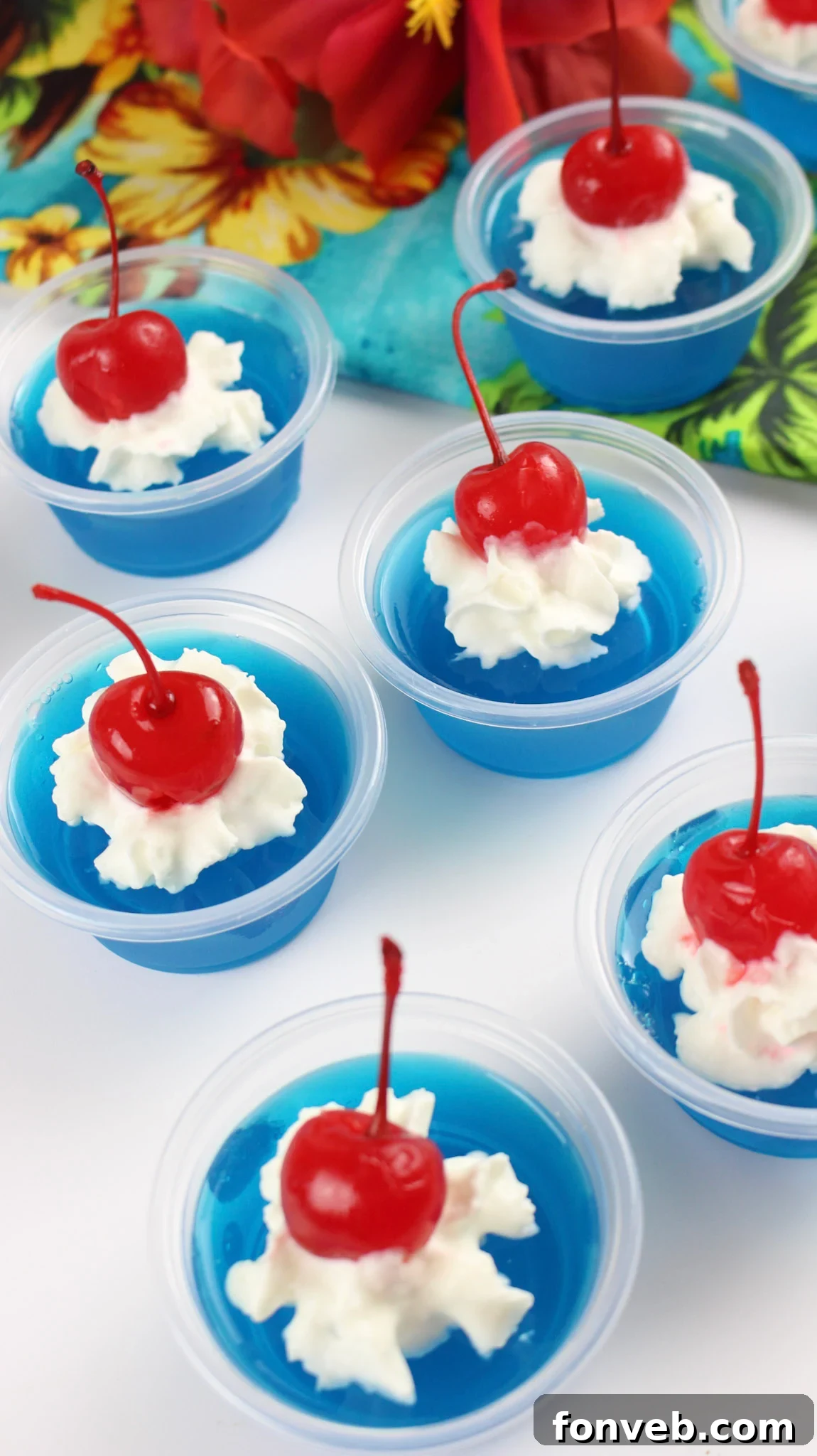 A closer view of a Blue Hawaiian Jello Shot, highlighting the creamy whipped topping and a bright red cherry, indicating a delicious dessert shot.