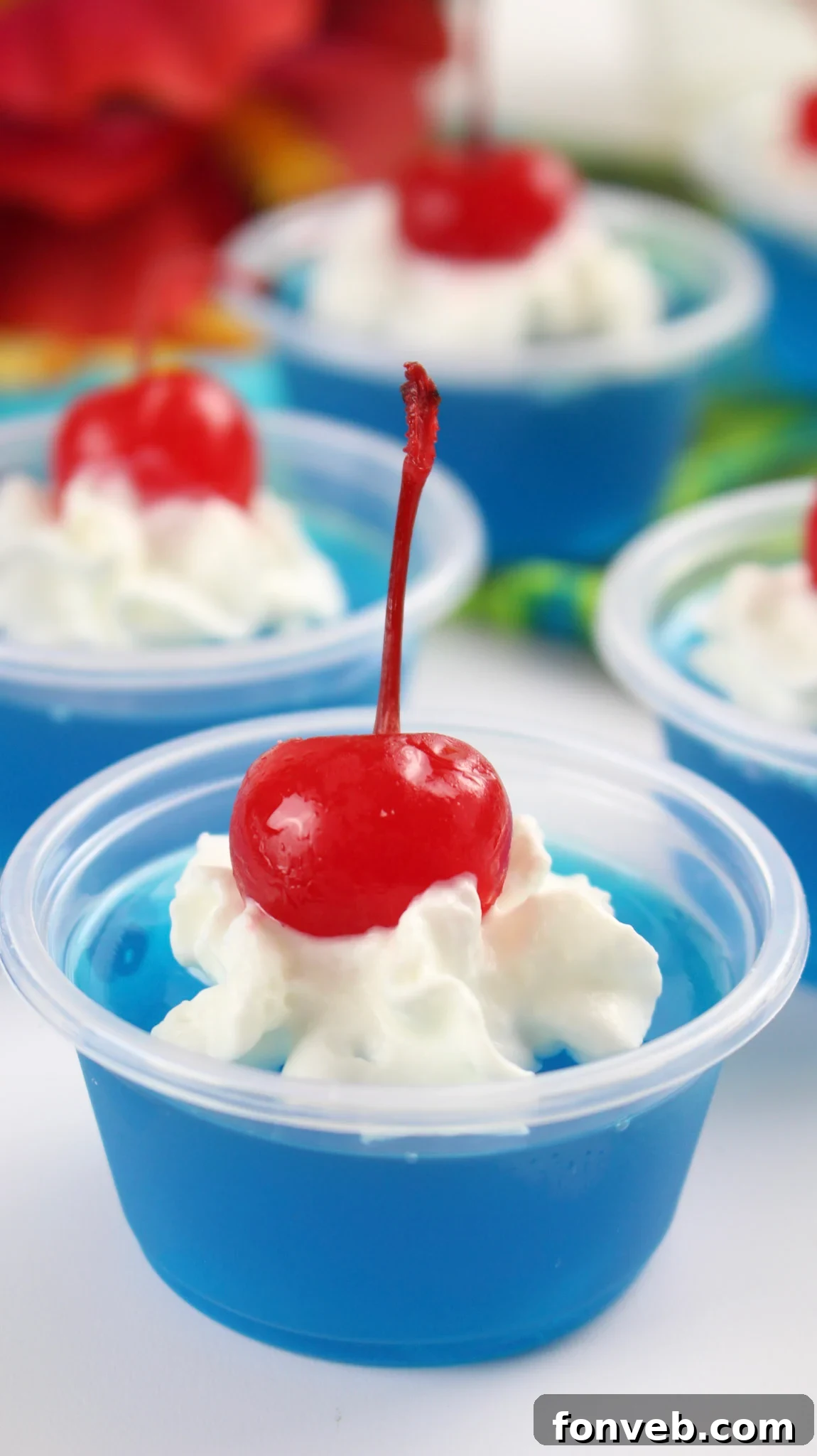 A top-down view of Blue Hawaiian Jello Shots in small cups, garnished with whipped cream and cherries, highlighting their inviting appearance and readiness for enjoyment.