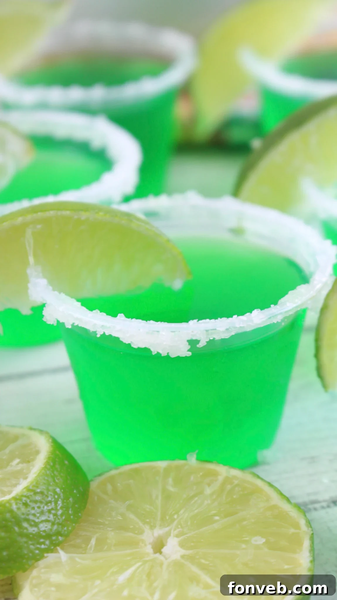 Vibrant green Margarita Jello Shots in small plastic cups, garnished with lime wedges and salt on the rim.
