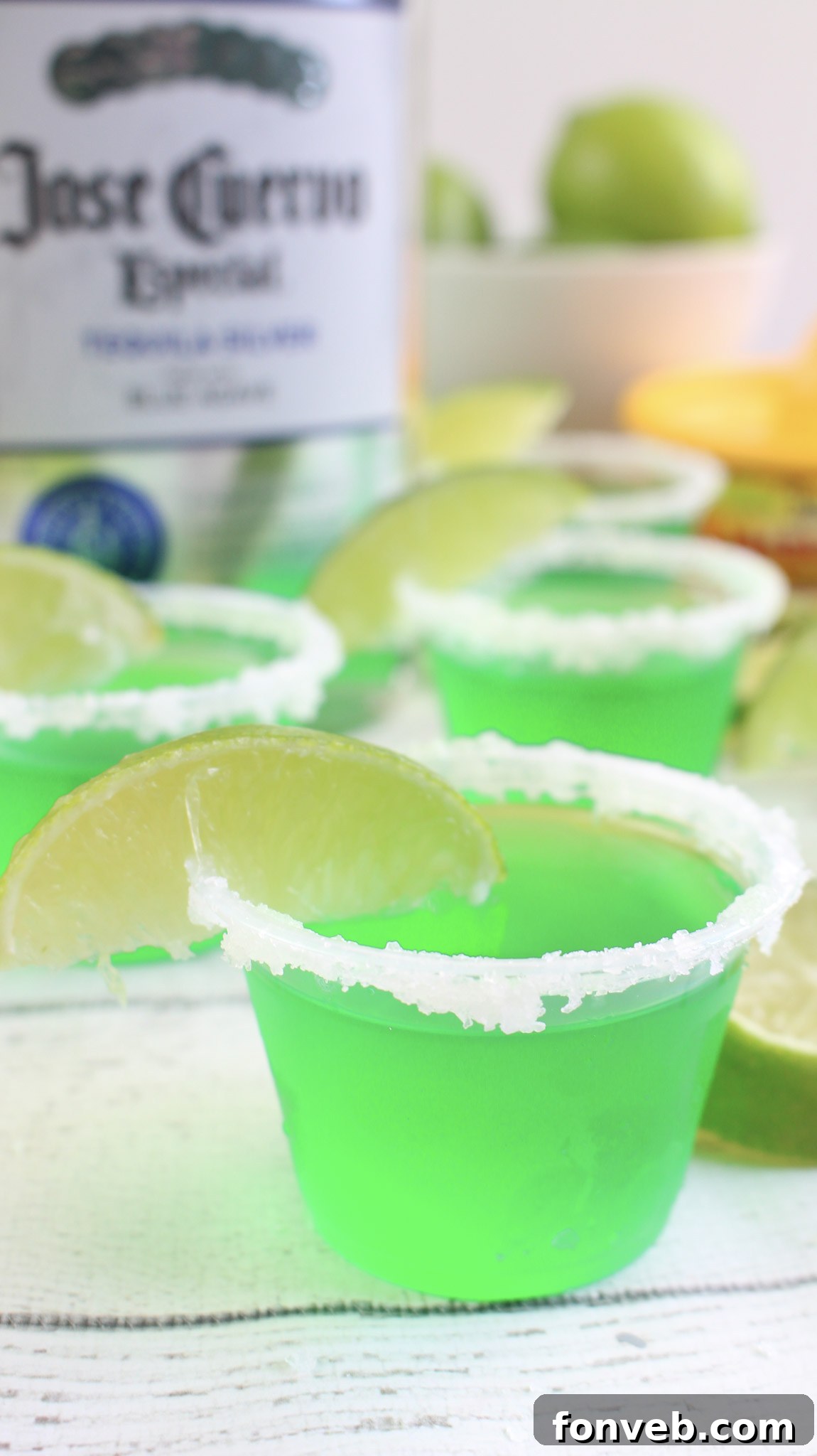 Hand holding a Margarita Jello Shot with a perfectly salted rim and lime wedge.