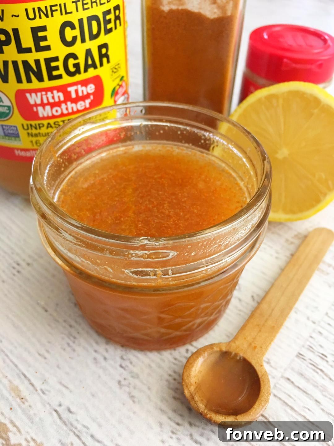 A glass bottle of homemade cough syrup surrounded by its natural ingredients: honey, lemons, ginger, and apple cider vinegar.
