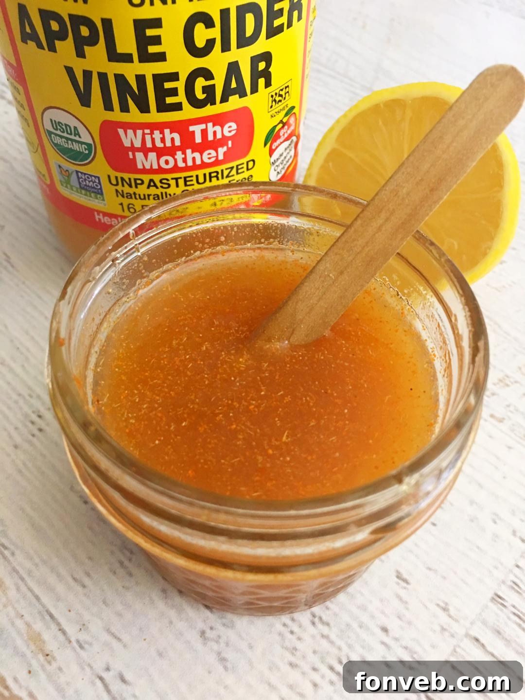 A bottle of homemade cough syrup, with fresh ginger, lemons, and cayenne pepper in the background.