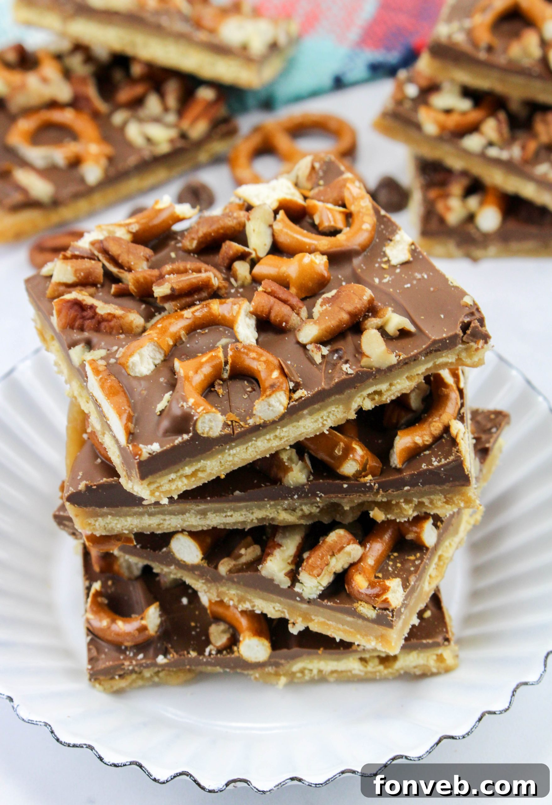 A large tray filled with rectangular Saltine Cracker Toffee pieces, glistening with chocolate and caramel, topped with chopped pretzels and pecans.