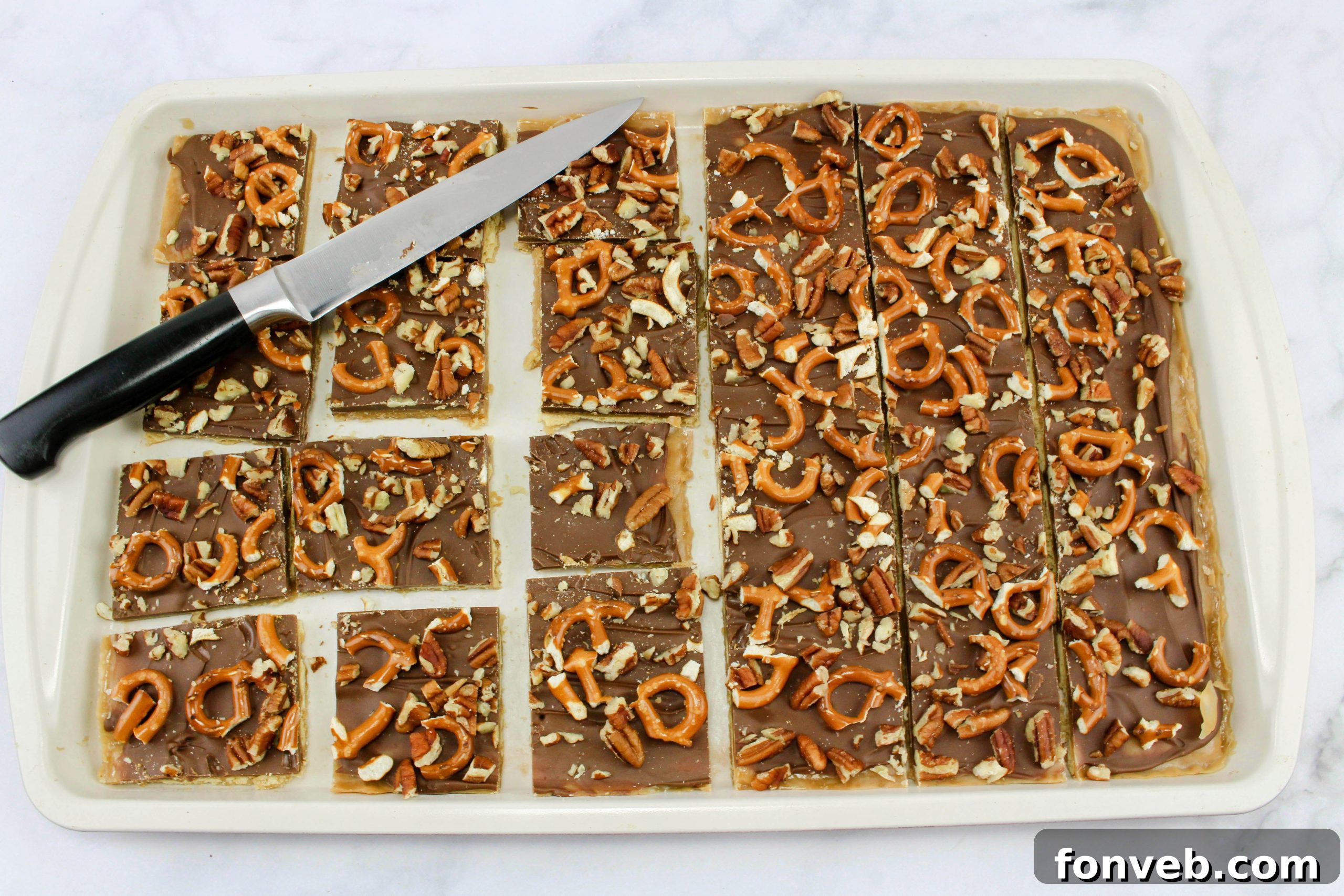 A close-up showing the chopped pretzels and pecans scattered over the chocolate layer, awaiting cooling and hardening.