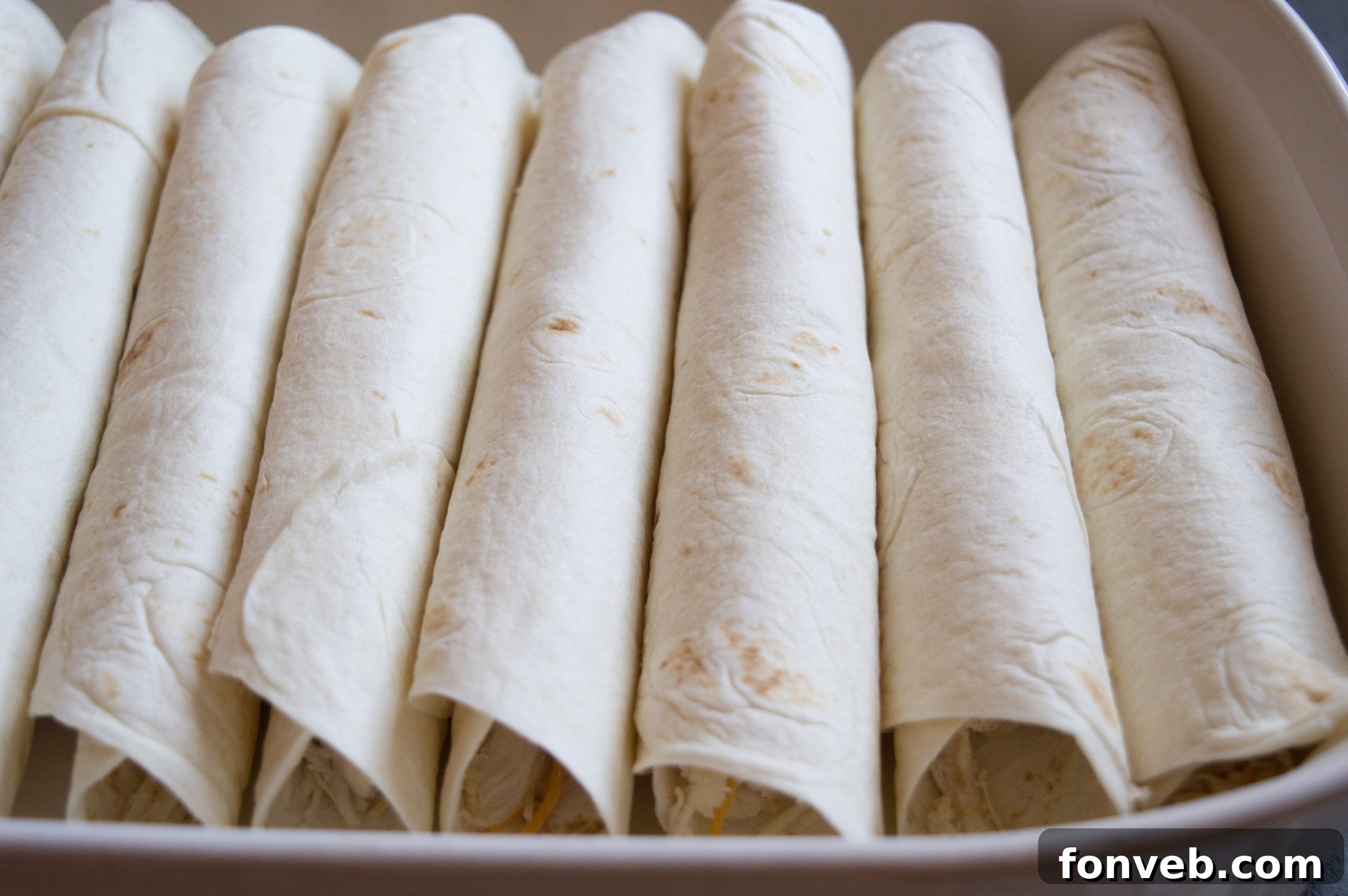 Top-down shot of a baking dish filled with golden-brown white chicken enchiladas, bubbling with cheese.