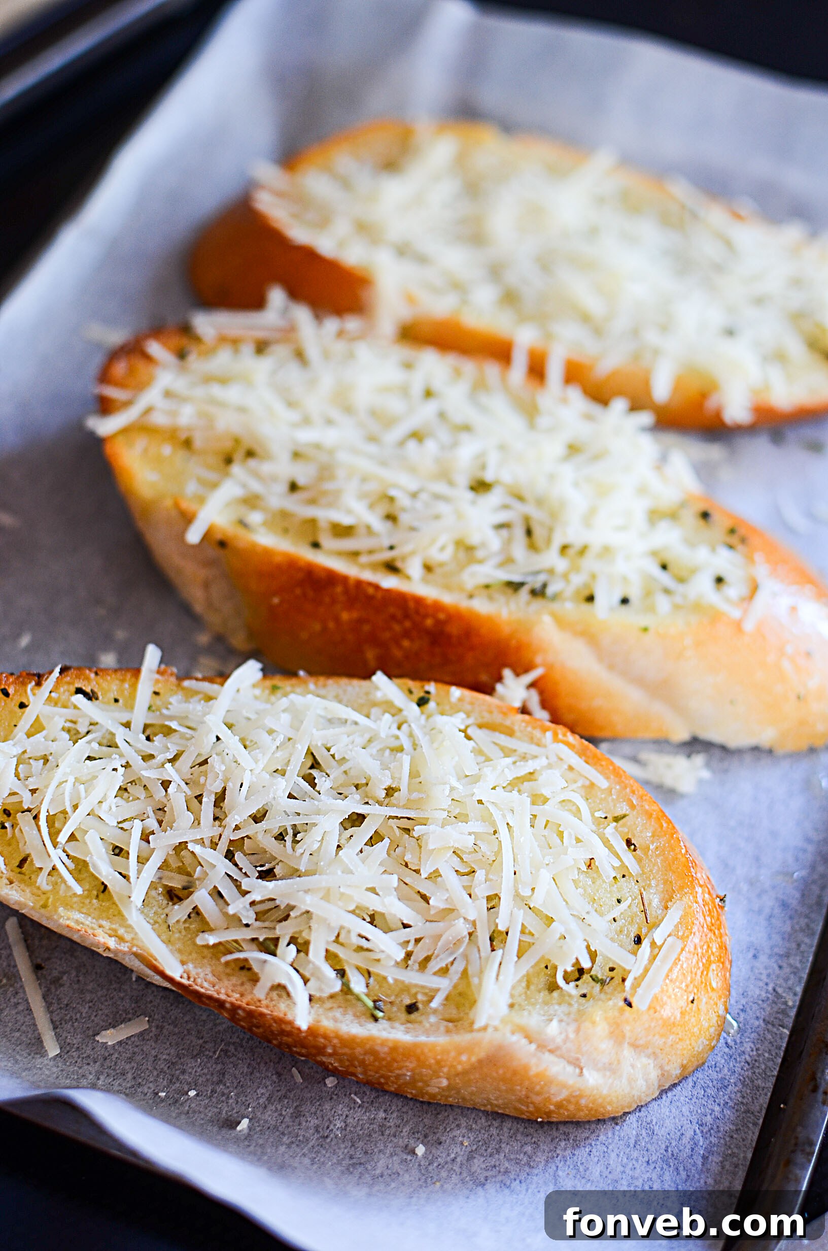 Garlic bread ingredients laid out: a loaf of French bread, fresh garlic cloves, butter, and parmesan cheese