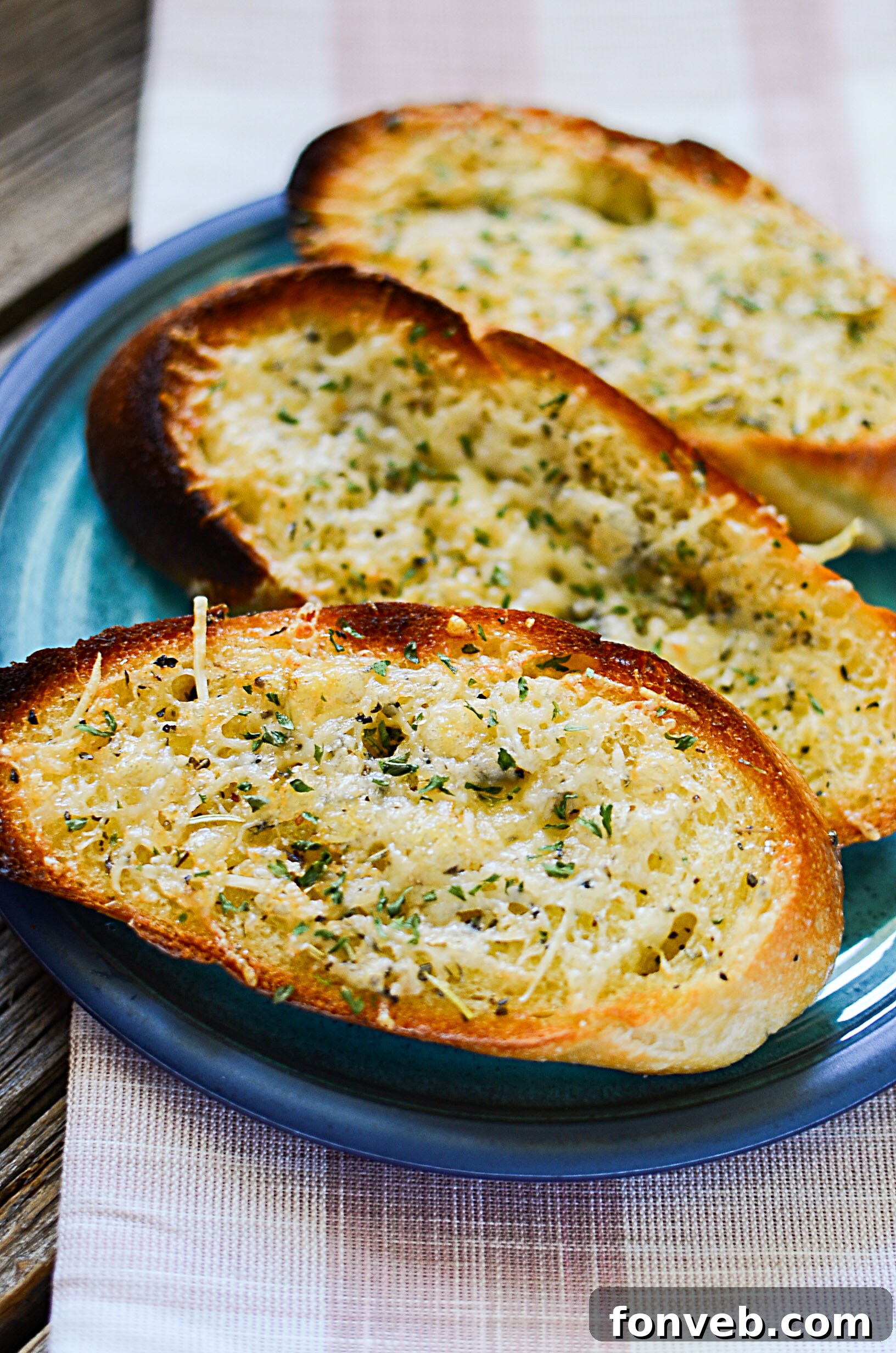 A rustic cutting board holding several slices of homemade garlic parmesan bread, ready to eat