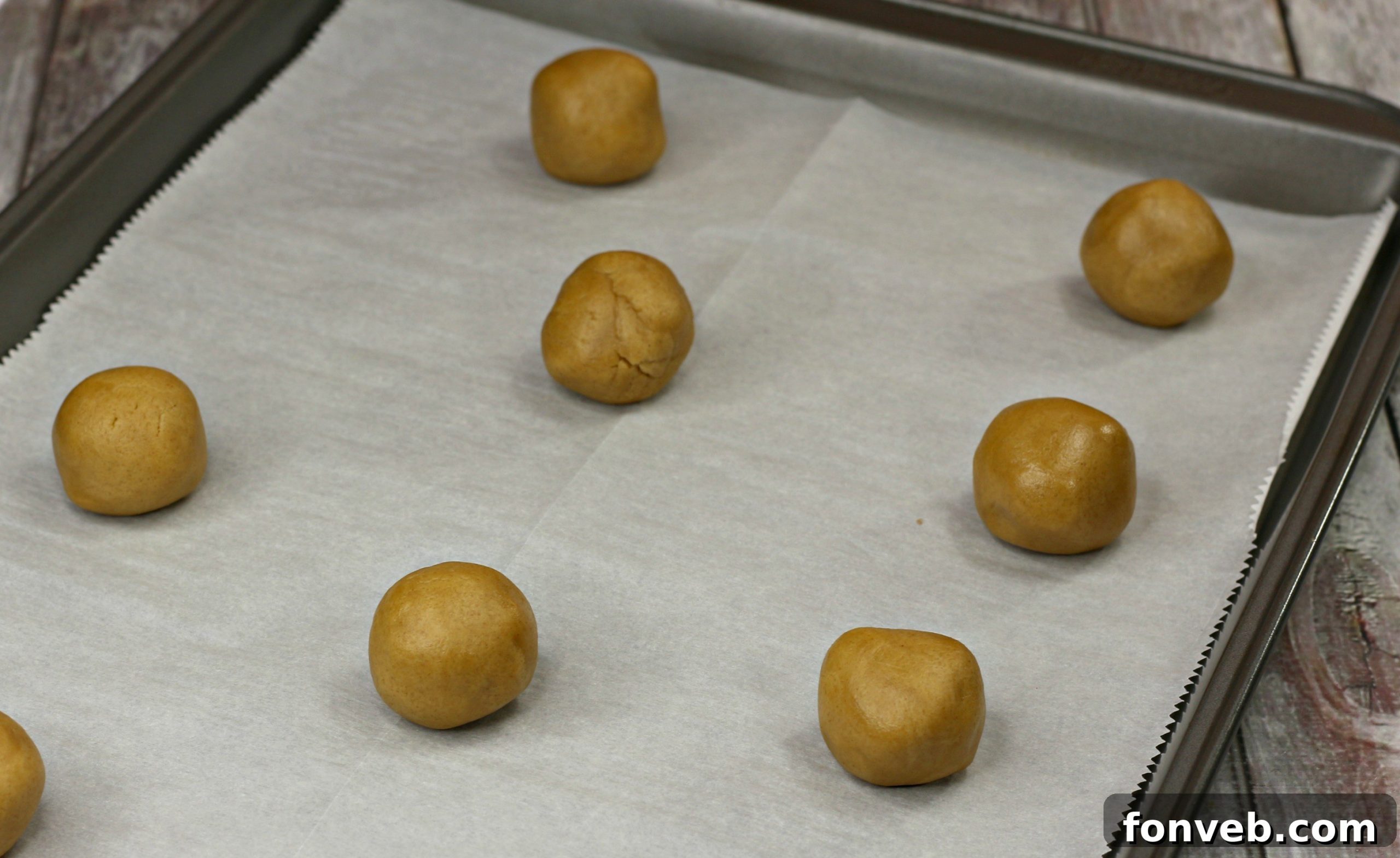 Close-up of baked peanut butter cookies arranged on a baking sheet, showing their signature peanut shape and criss-cross fork marks.