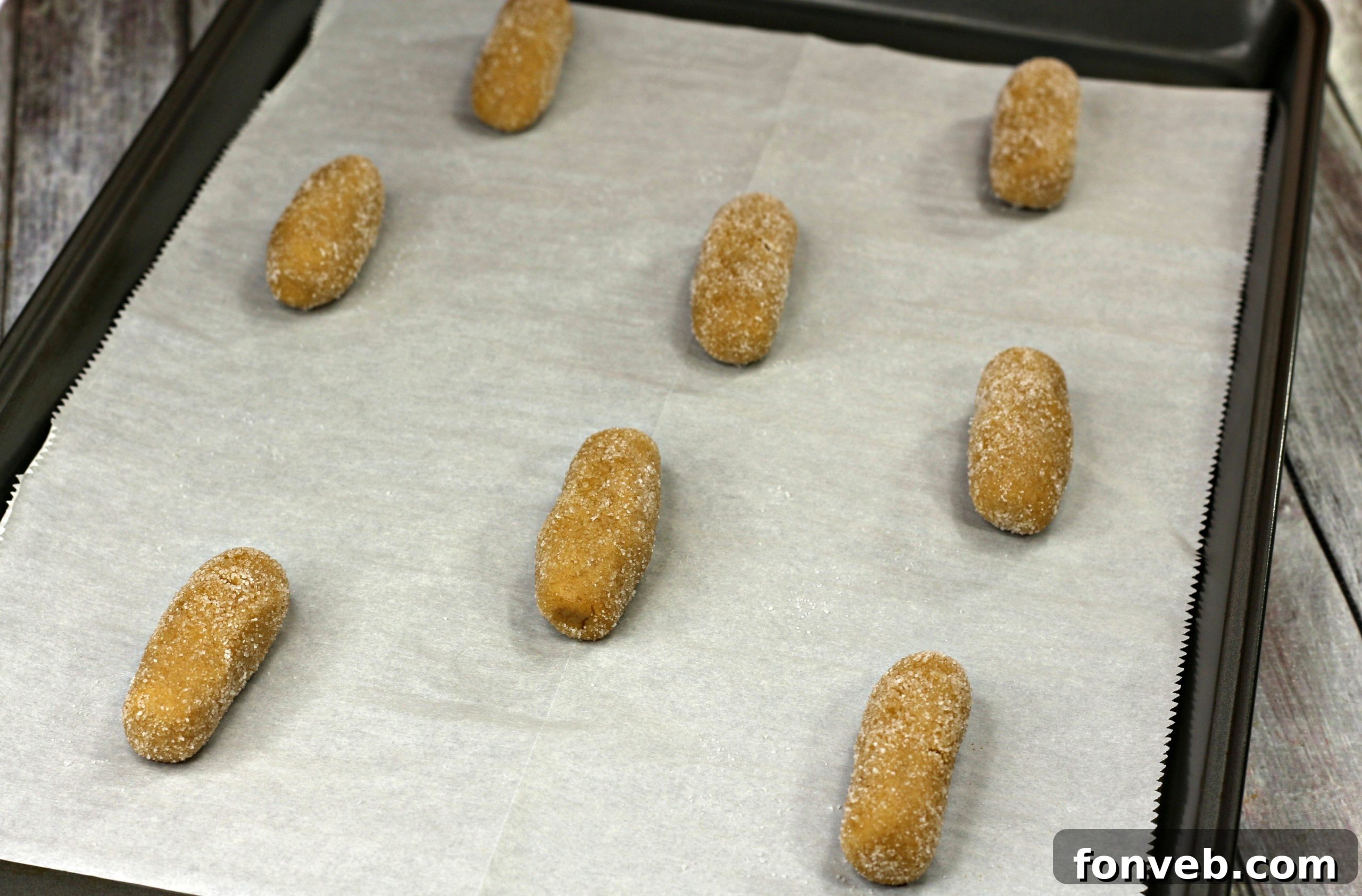 Peanut butter cookie dough logs being spaced out evenly on a parchment-lined baking sheet before baking.