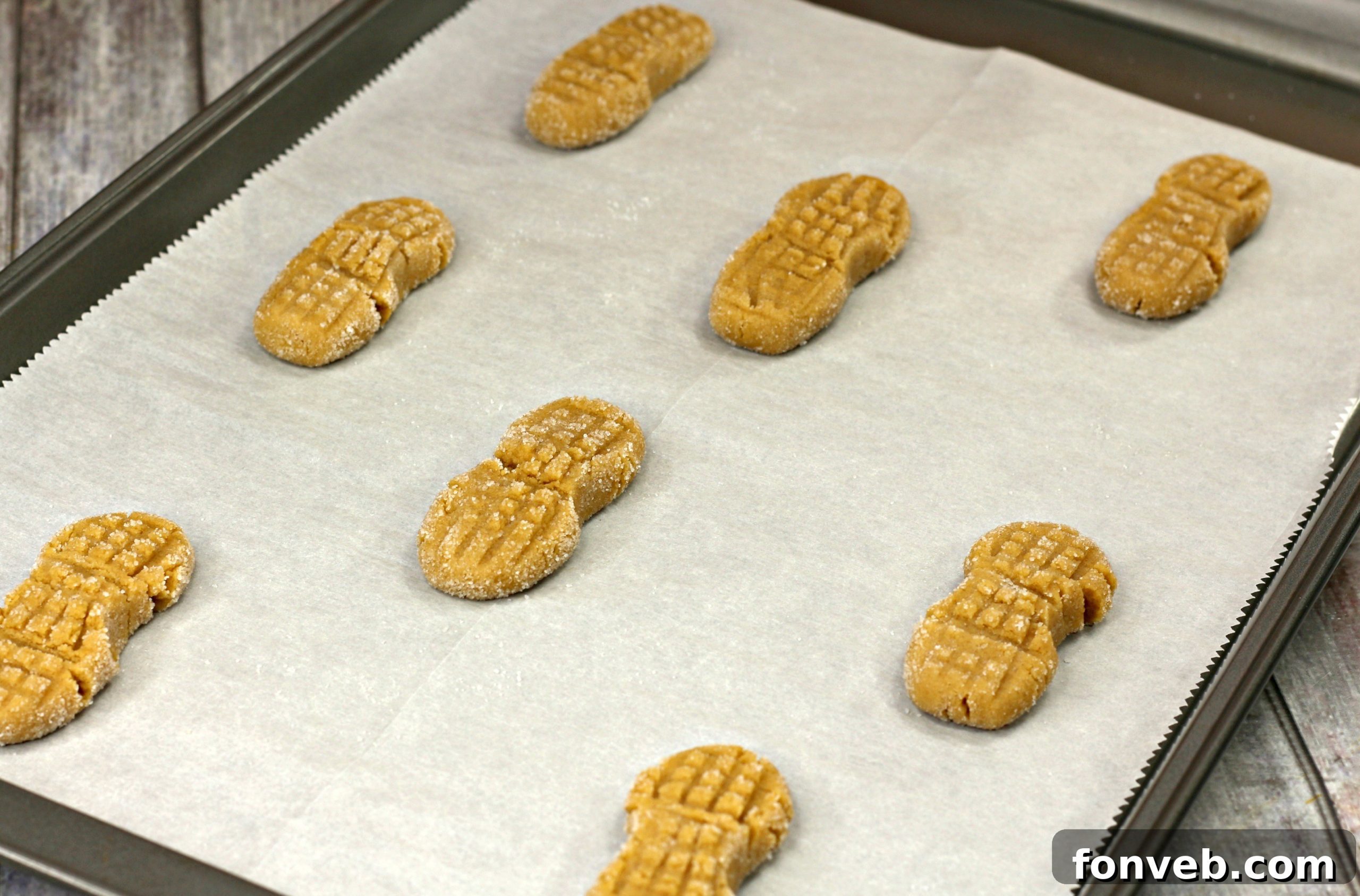 Close-up of peanut butter cookie dough logs being rolled evenly in granulated sugar by hand, creating a sweet coating.