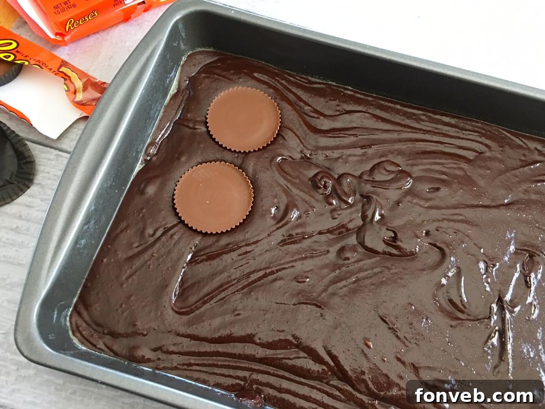 Children's hands gently pressing Reese's Peanut Butter Cups into brownie batter in a baking pan, a fun family activity.