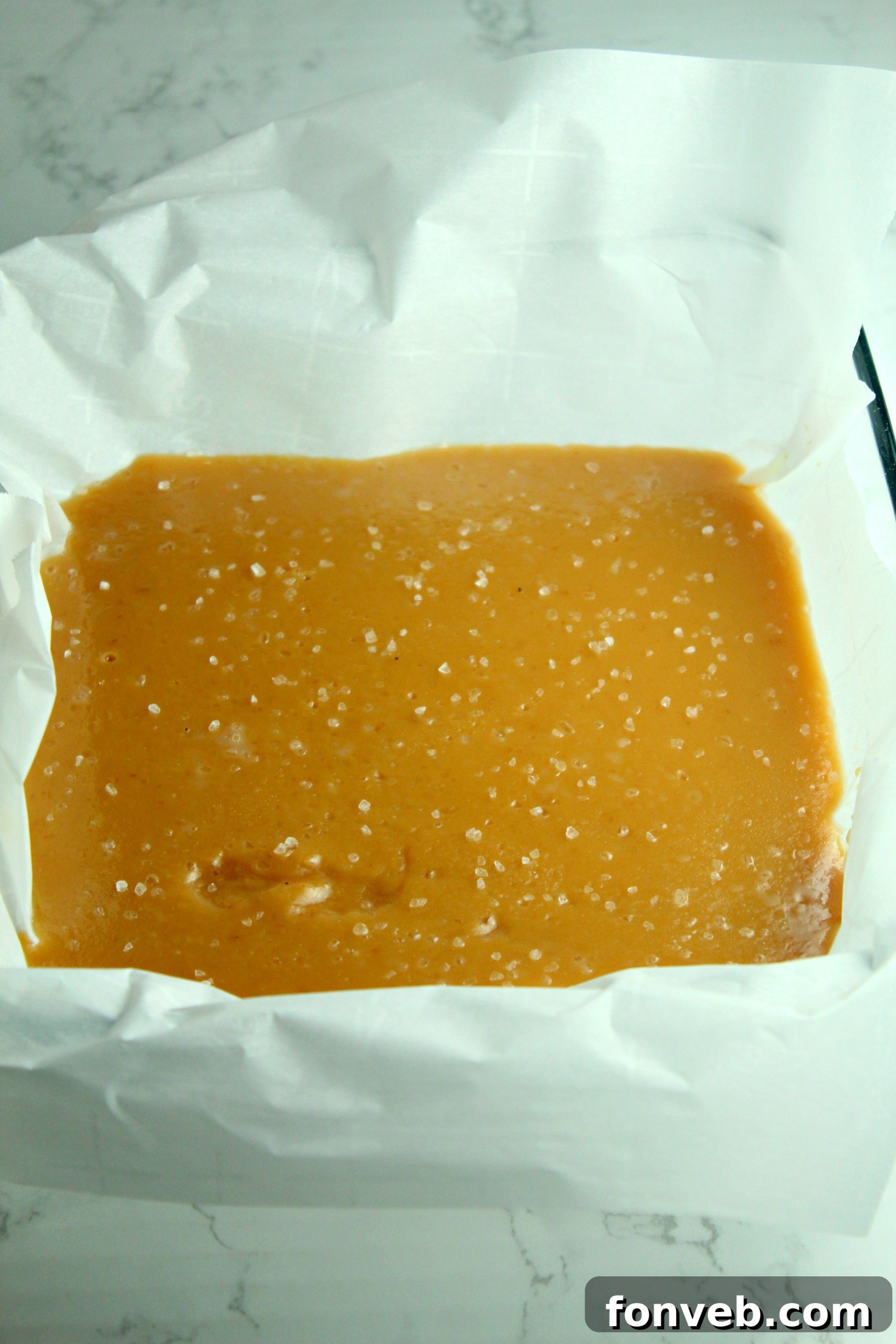 Handcrafted Salted Caramel Bliss 4 A hand peeling back parchment paper to reveal a tray of homemade salted caramels.