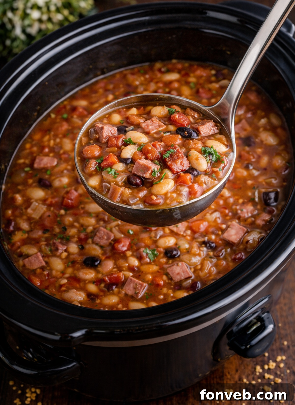 Set It and Forget It Ham and Bean Soup 7 A spoon lifting a spoonful of Slow Cooker Ham and Bean Soup from a black slow cooker