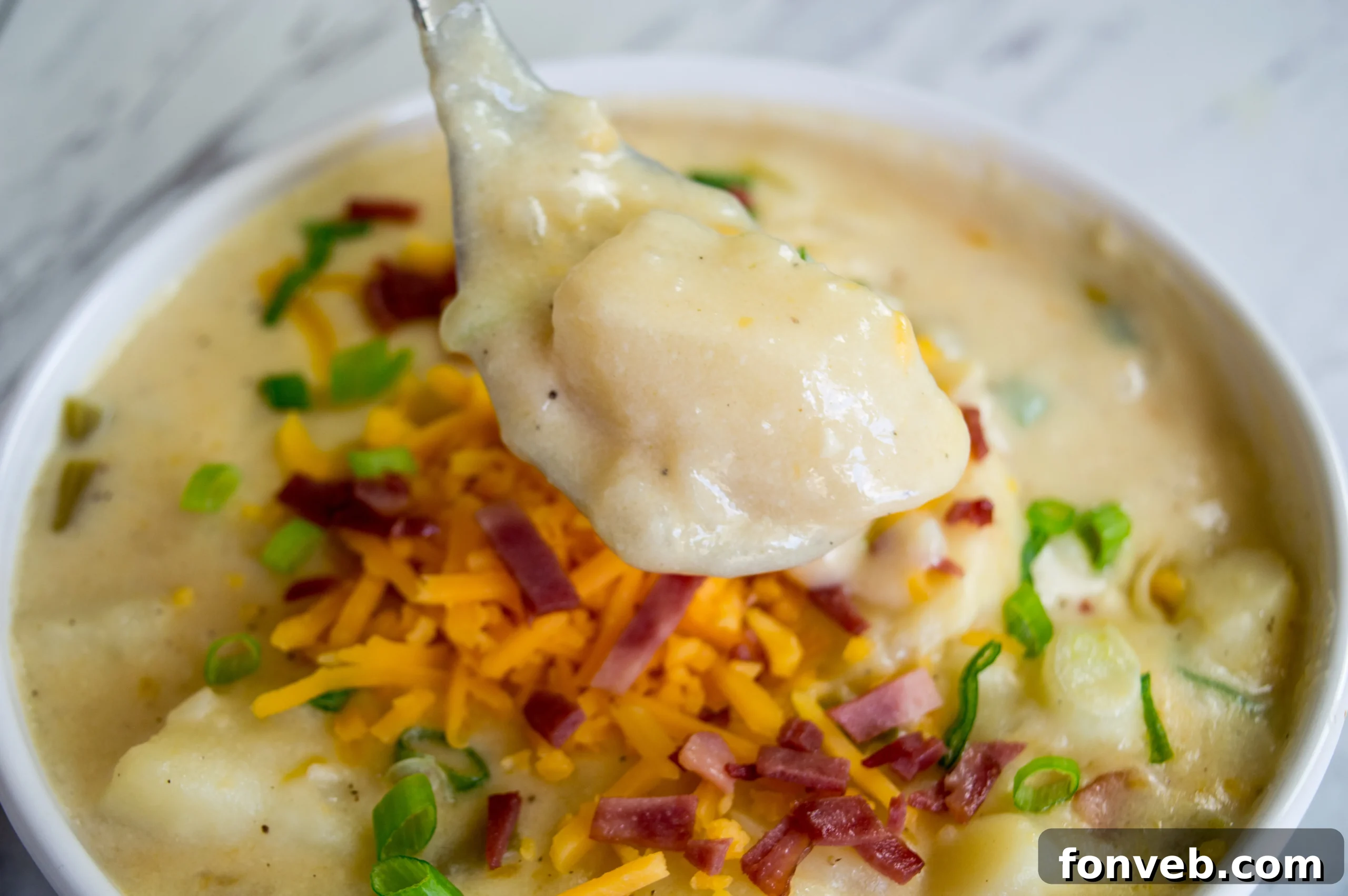 A large bowl of creamy loaded potato soup, topped with crispy bacon bits, melted cheddar cheese, and fresh green onions.