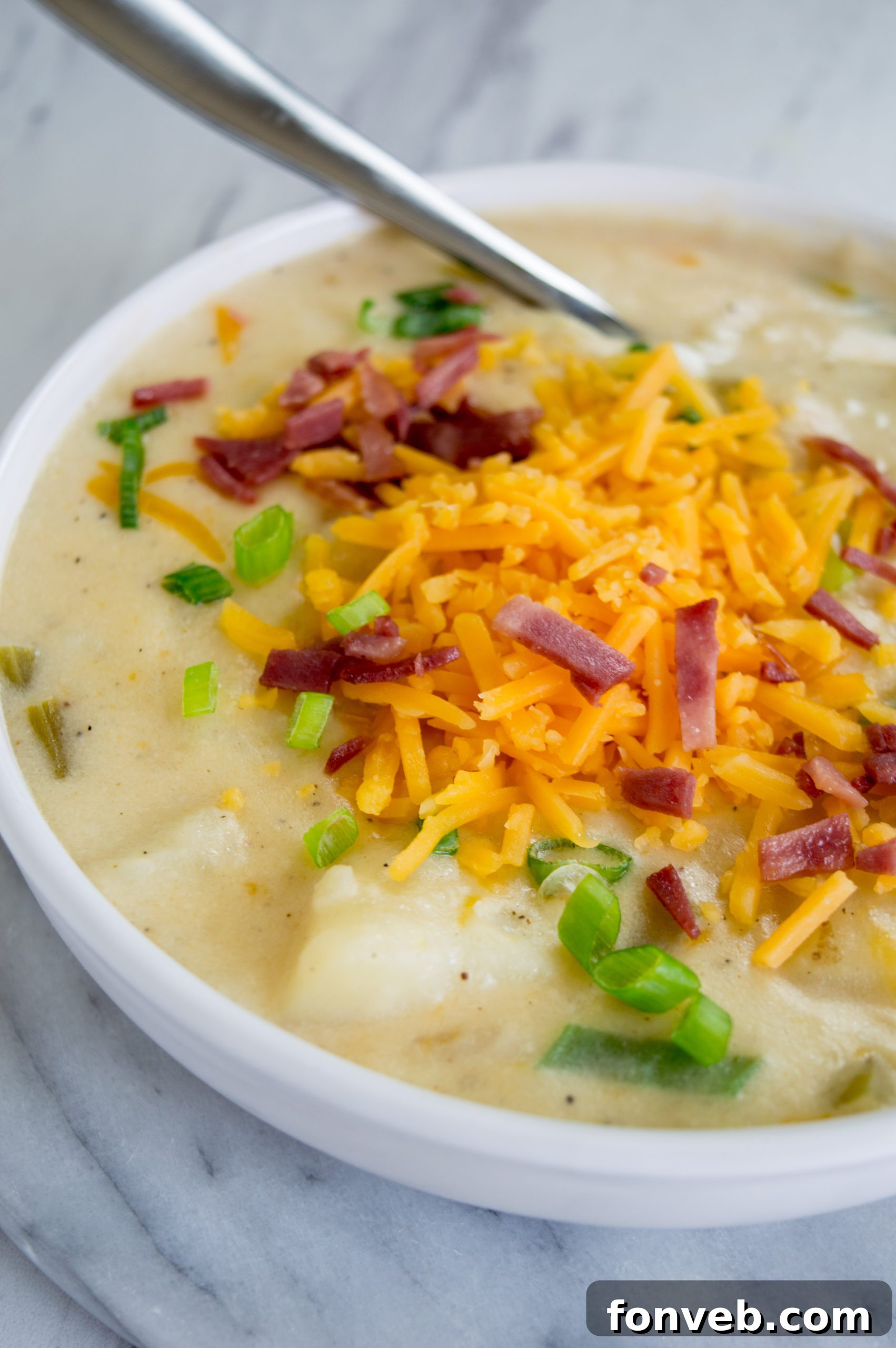 Close-up of a spoon scooping a portion of rich and creamy loaded potato soup, highlighting the tender potato chunks and melted cheese.