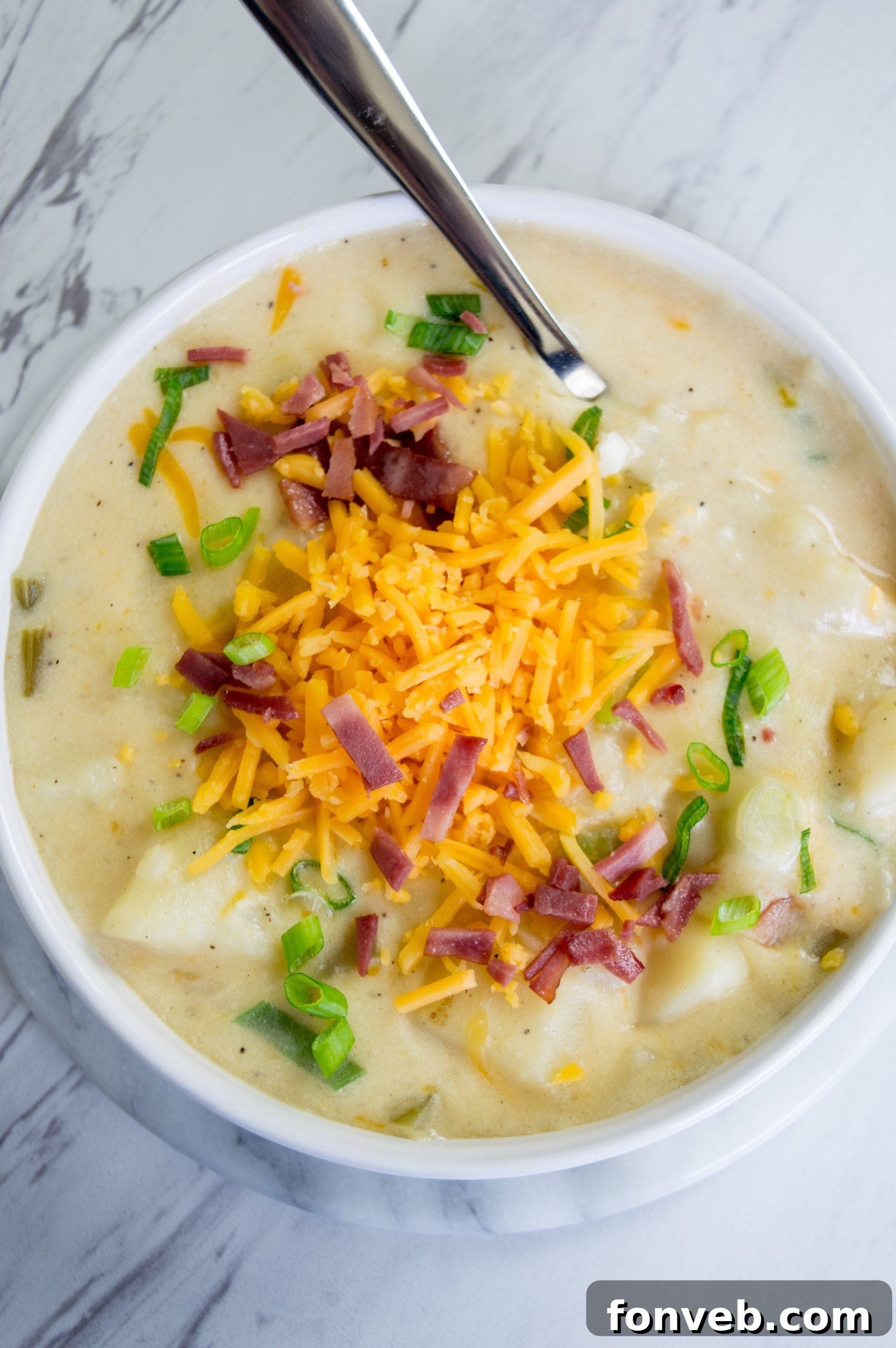 A beautifully presented bowl of loaded potato soup, generously garnished with crispy bacon bits, shredded cheddar cheese, and vibrant green onions.