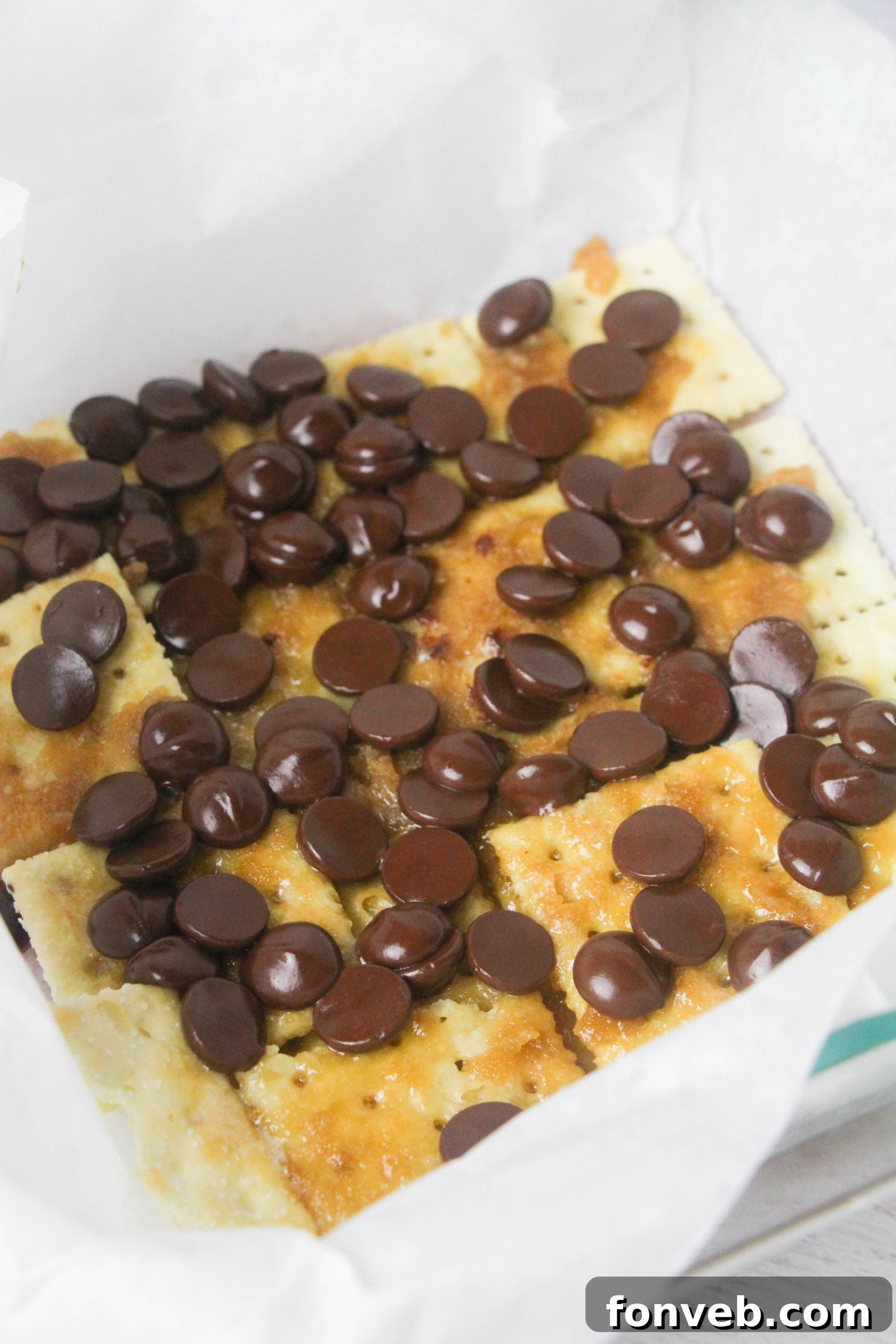 Several pieces of Christmas Crack, featuring milk chocolate and M&Ms, stacked artfully on a white plate with a festive background.