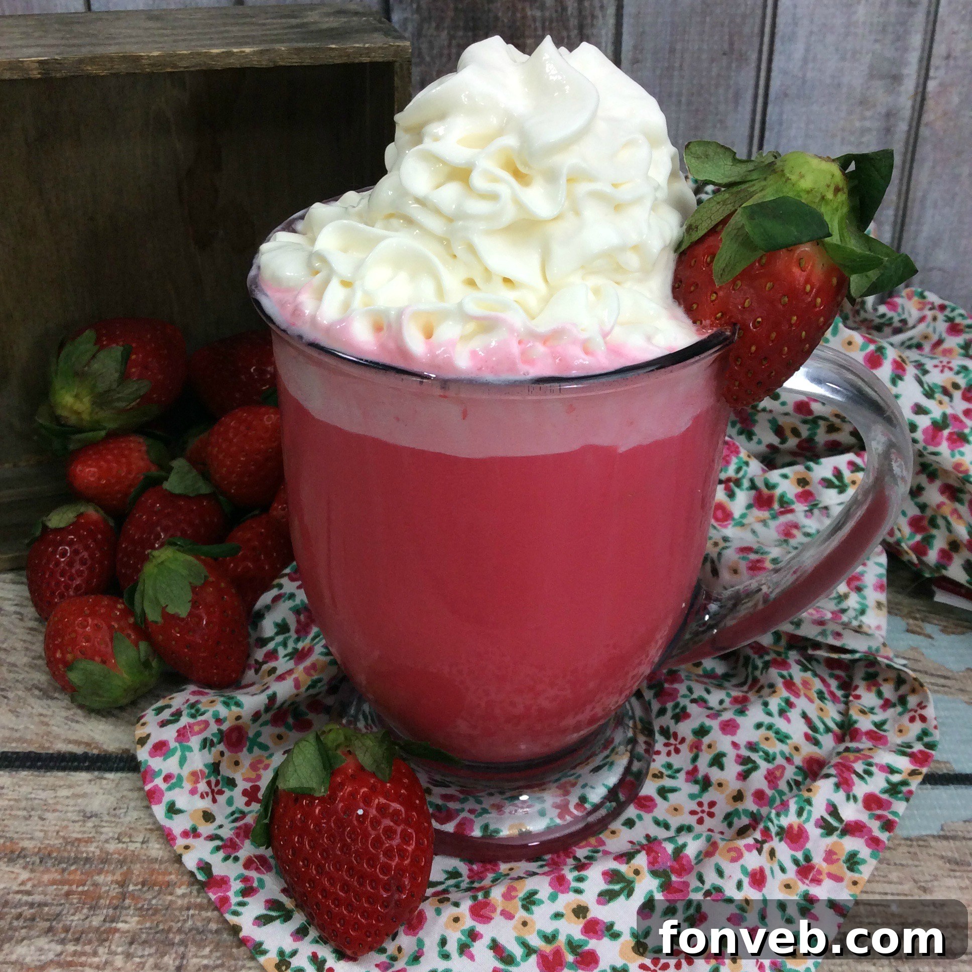 A warm mug of Strawberry White Hot Cocoa topped with whipped cream and fresh strawberries