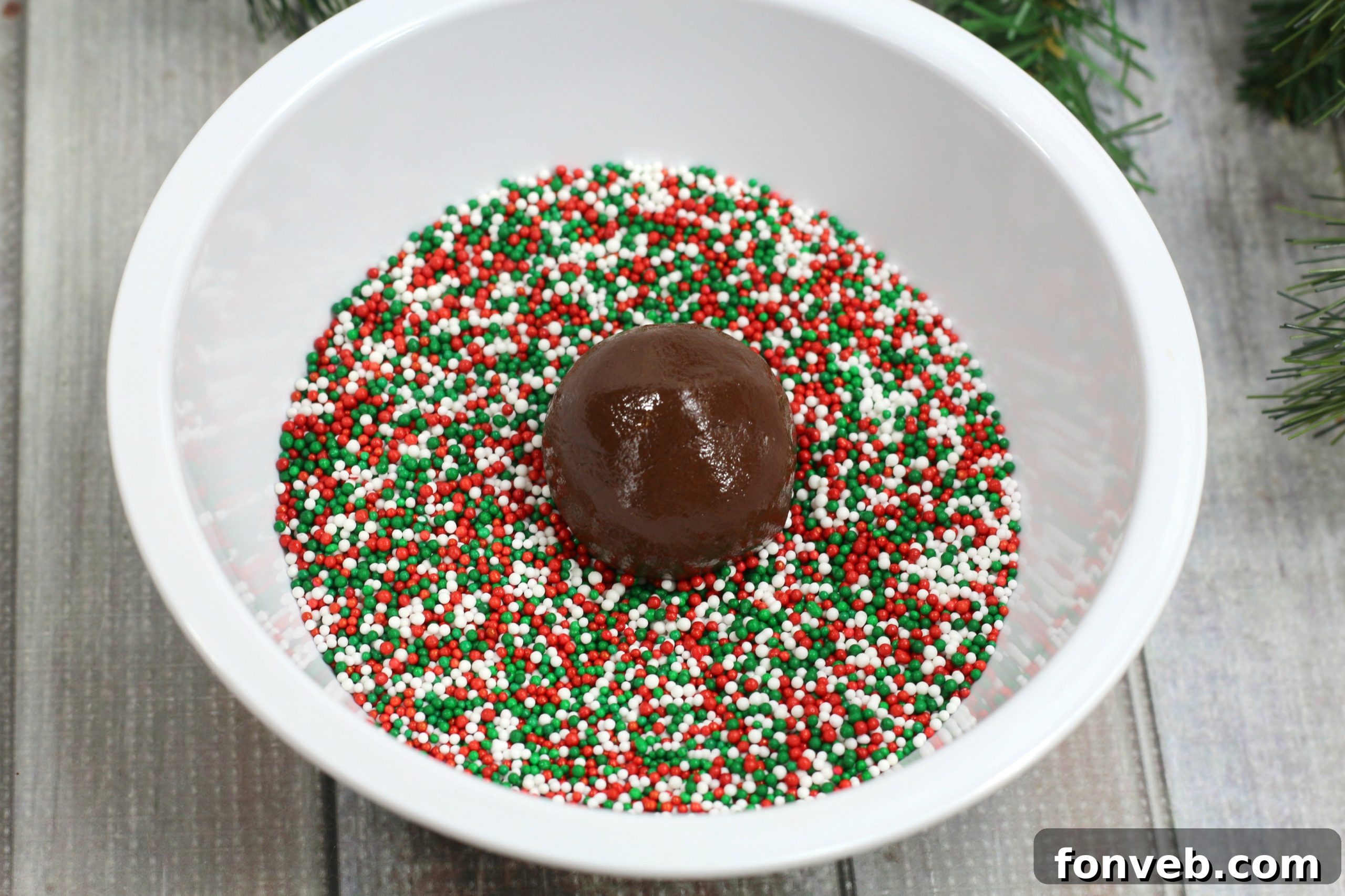 Hand rolling a chocolate Kahlua truffle in a bowl of festive red, green, and white sprinkles.
