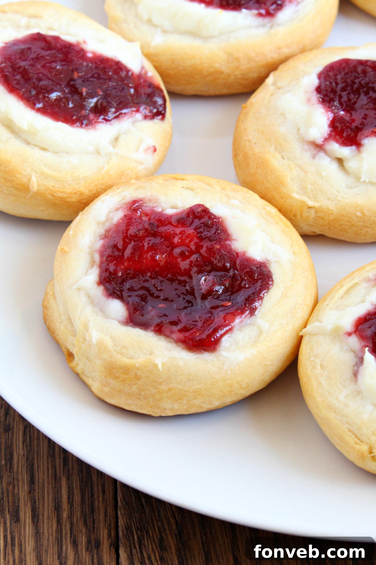 Raw crescent dough circles filled with cream cheese and raspberry jam, ready for baking.