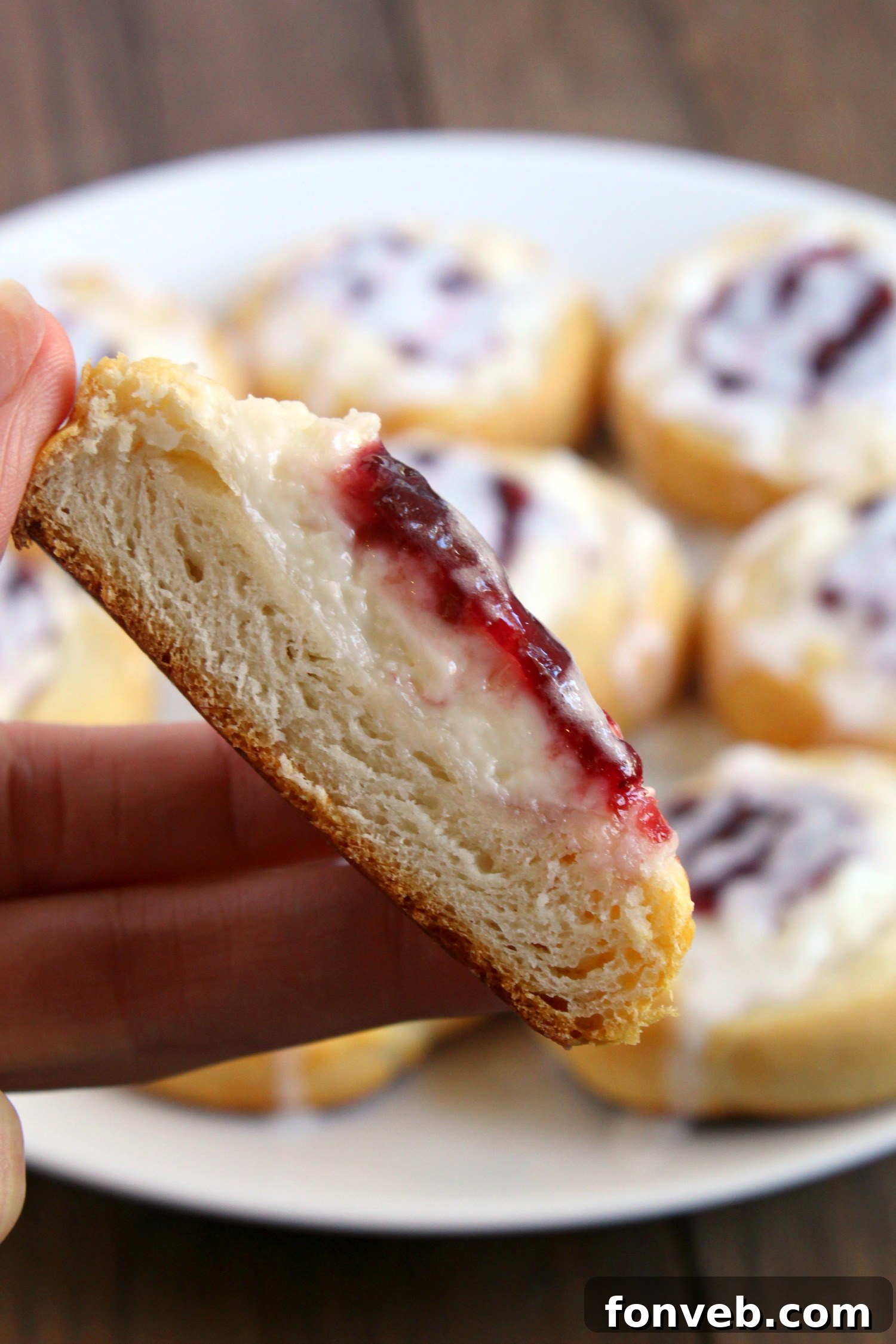 A close-up of a raspberry cream cheese danish being held, showing the texture and filling.