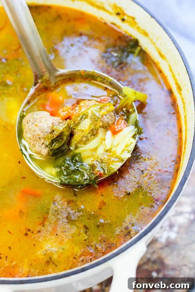 Rustic Tuscan Meatball Soup 2 A large bowl of hearty Tuscan Meatball Soup with baked meatballs, orzo pasta, and vibrant green kale, garnished with fresh herbs, served on a wooden table.