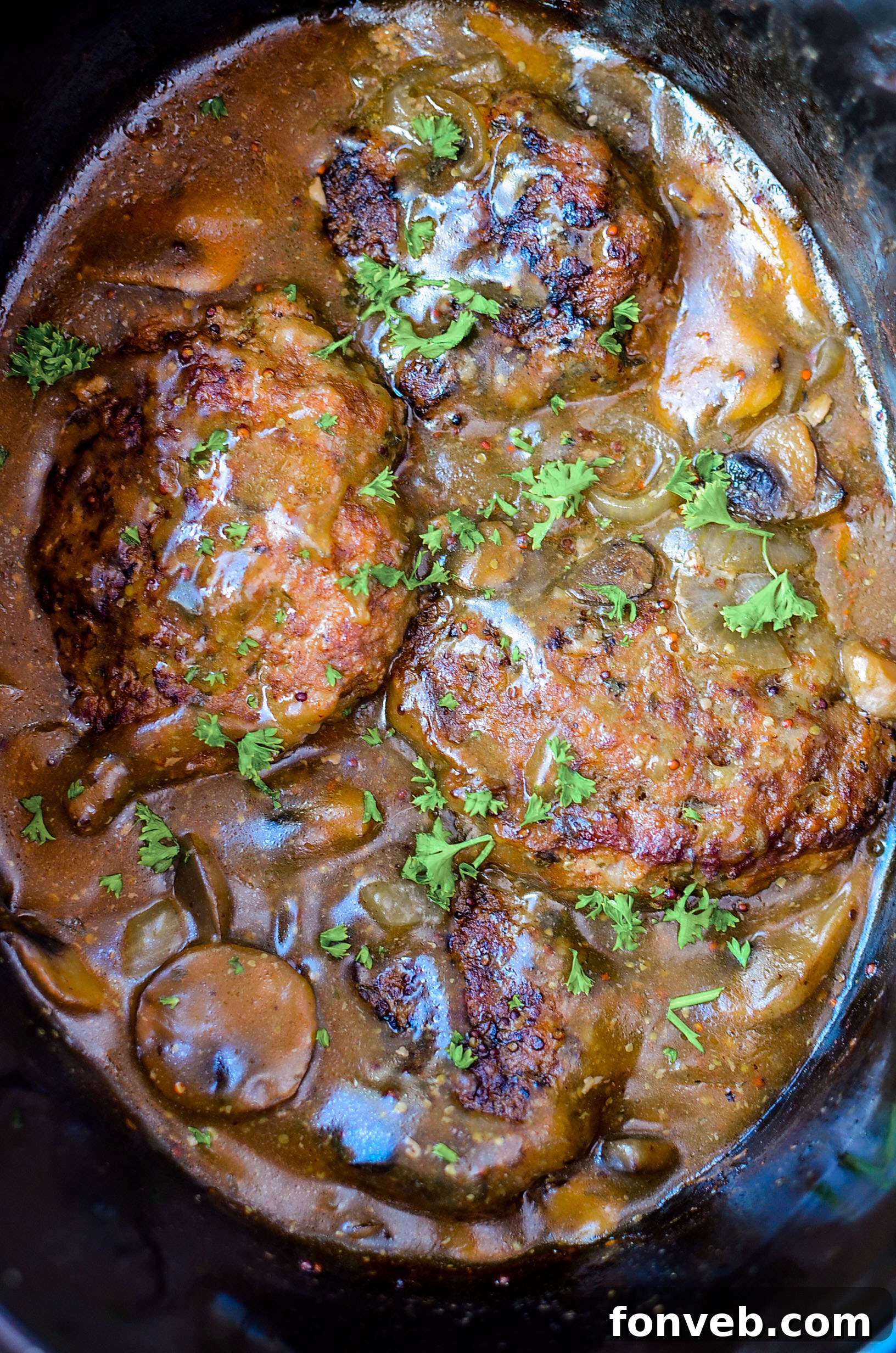 A serving of Slow Cooker Salisbury Steak on a white plate, showcasing the thick gravy and tender patty, garnished with fresh parsley.