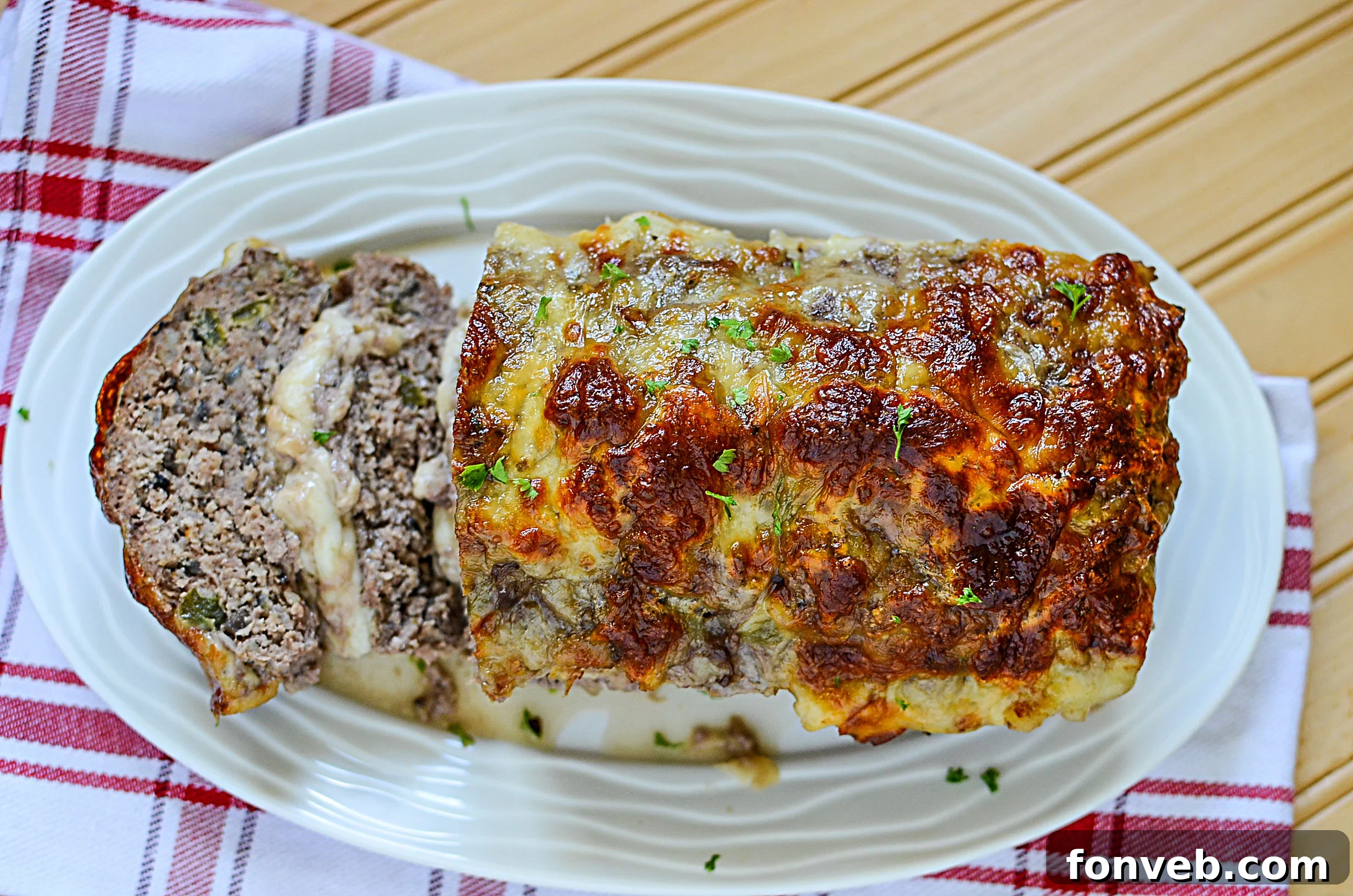 A hand holding a slice of Philly Cheesesteak Meatloaf, showing the gooey melted cheese inside