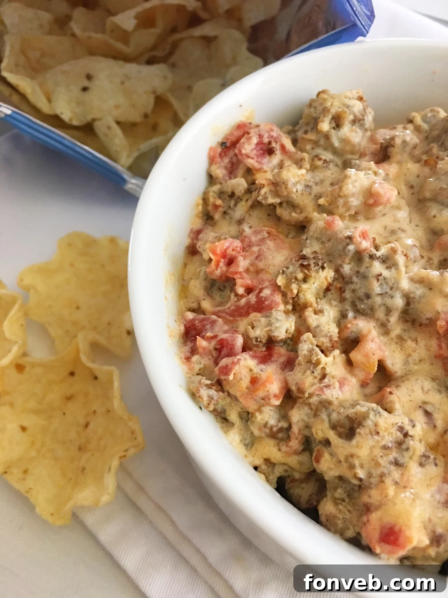 Mouthwatering Three-Ingredient Spicy Sausage Dip 2 Close-up of a bowl of creamy, orange-tinted spicy sausage dip, with a spoon nestled in it, ready for serving.