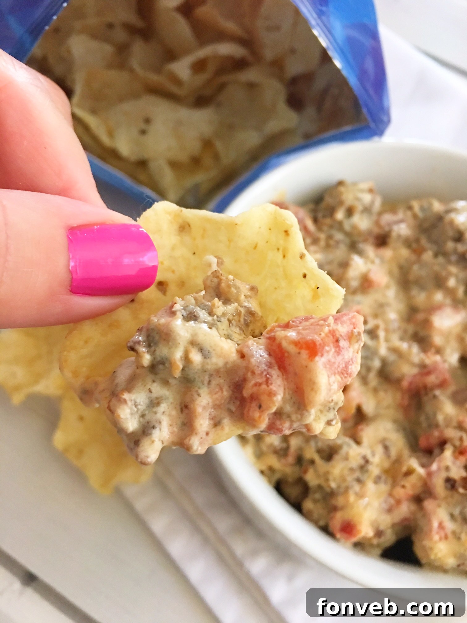 Mouthwatering Three-Ingredient Spicy Sausage Dip 5 A close-up of a person scooping the spicy sausage dip onto a chip, highlighting its creamy texture.
