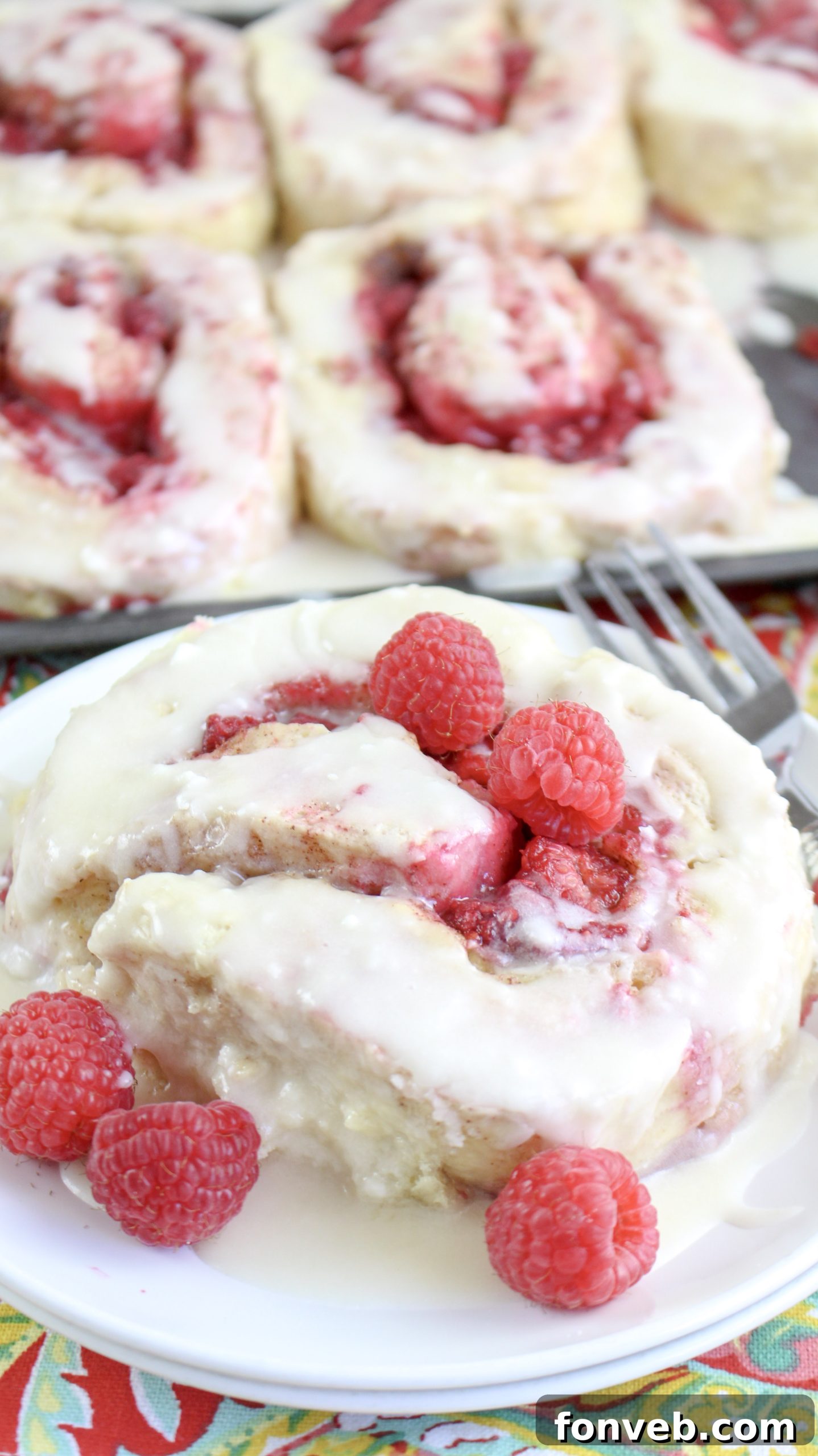 Velvet Raspberry Cinnamon Rolls 2 Close-up of freshly baked raspberry cinnamon rolls, glistening with warm icing and topped with fresh raspberries, ready to be served.