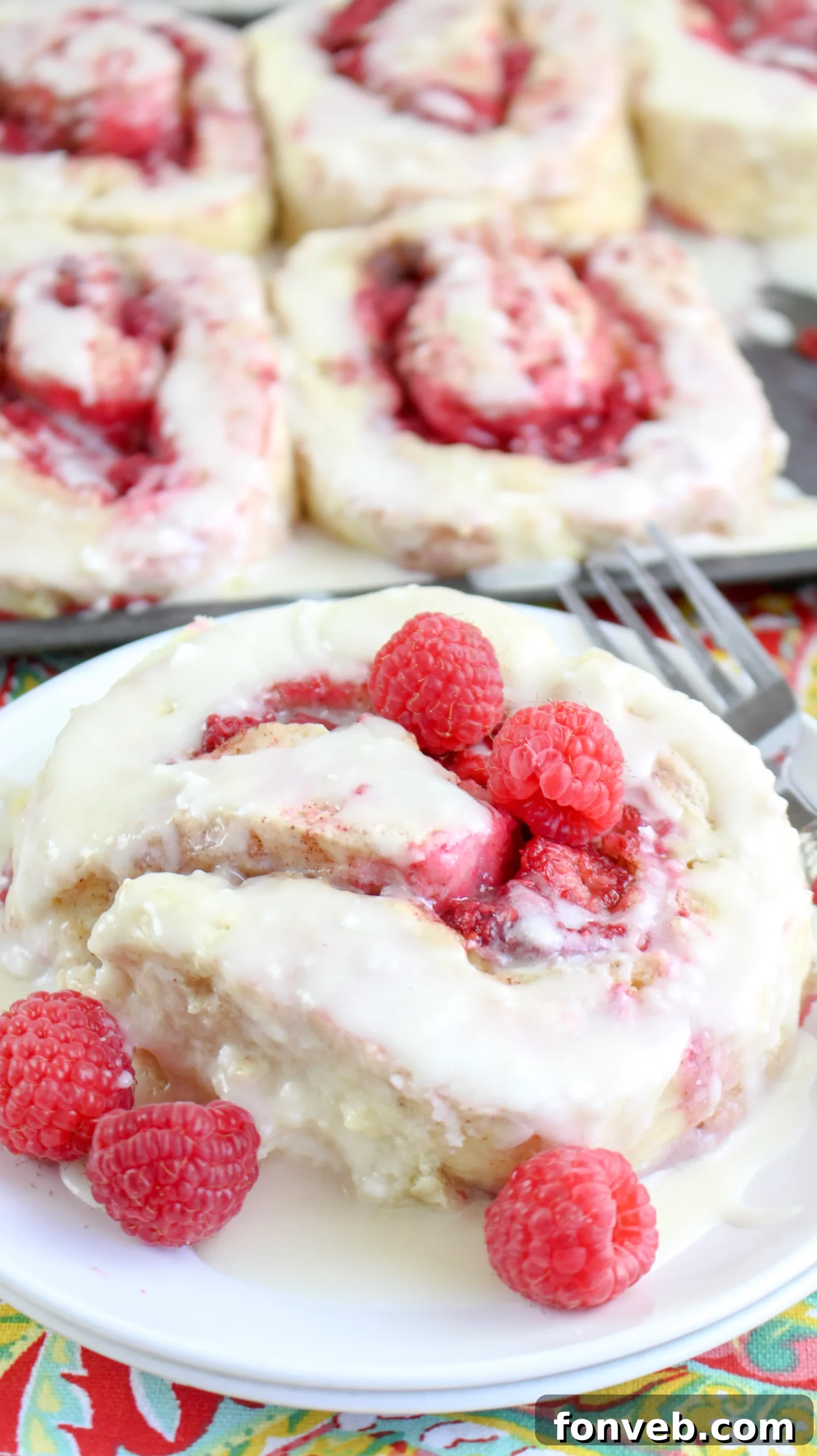 Velvet Raspberry Cinnamon Rolls 11 A stack of three raspberry cinnamon rolls, freshly iced and decorated with fresh raspberries, symbolizing abundance and deliciousness.