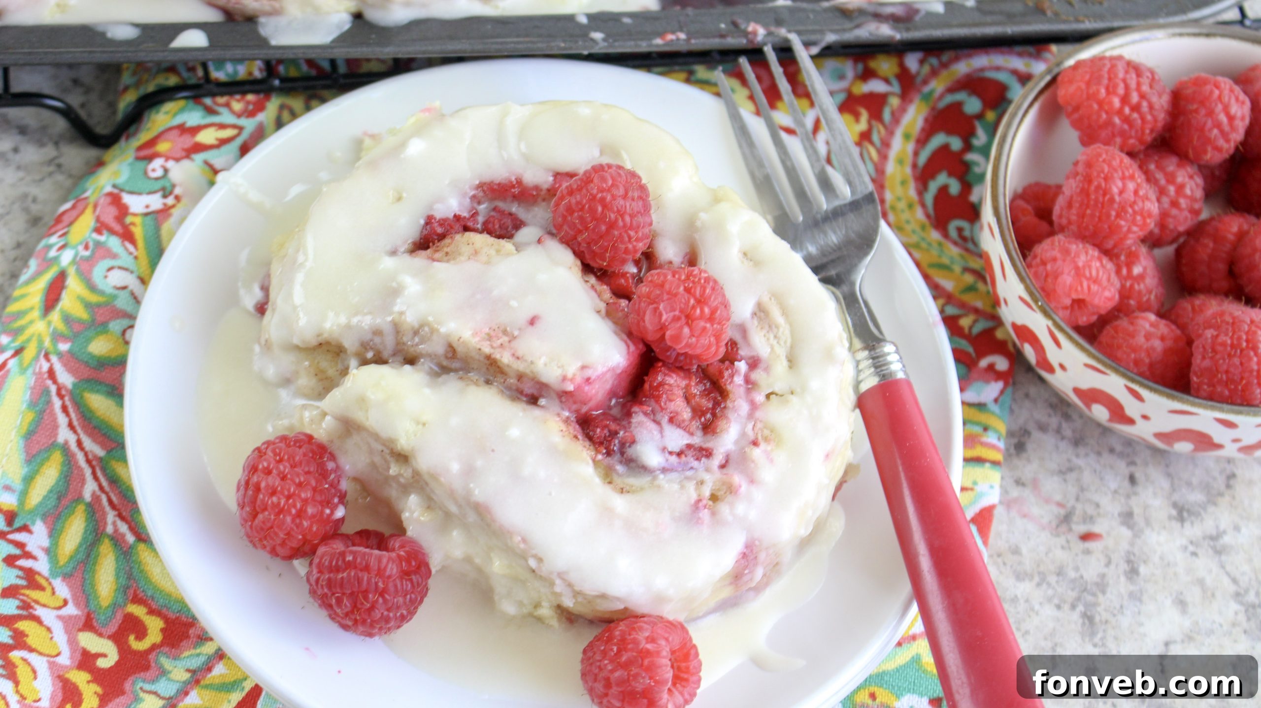 Velvet Raspberry Cinnamon Rolls 12 A single raspberry cinnamon roll being gently pulled apart, revealing the soft, layered dough and juicy raspberry filling within.