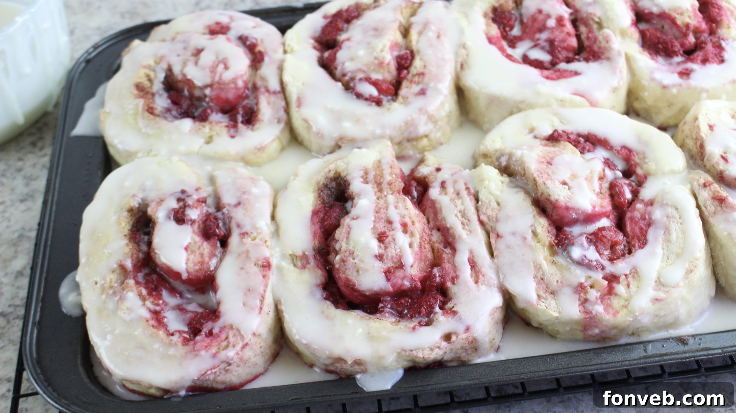 Velvet Raspberry Cinnamon Rolls 4 A close-up shot of several raspberry cinnamon rolls arranged neatly in a baking pan, showing the rich brown sugar and berry filling.