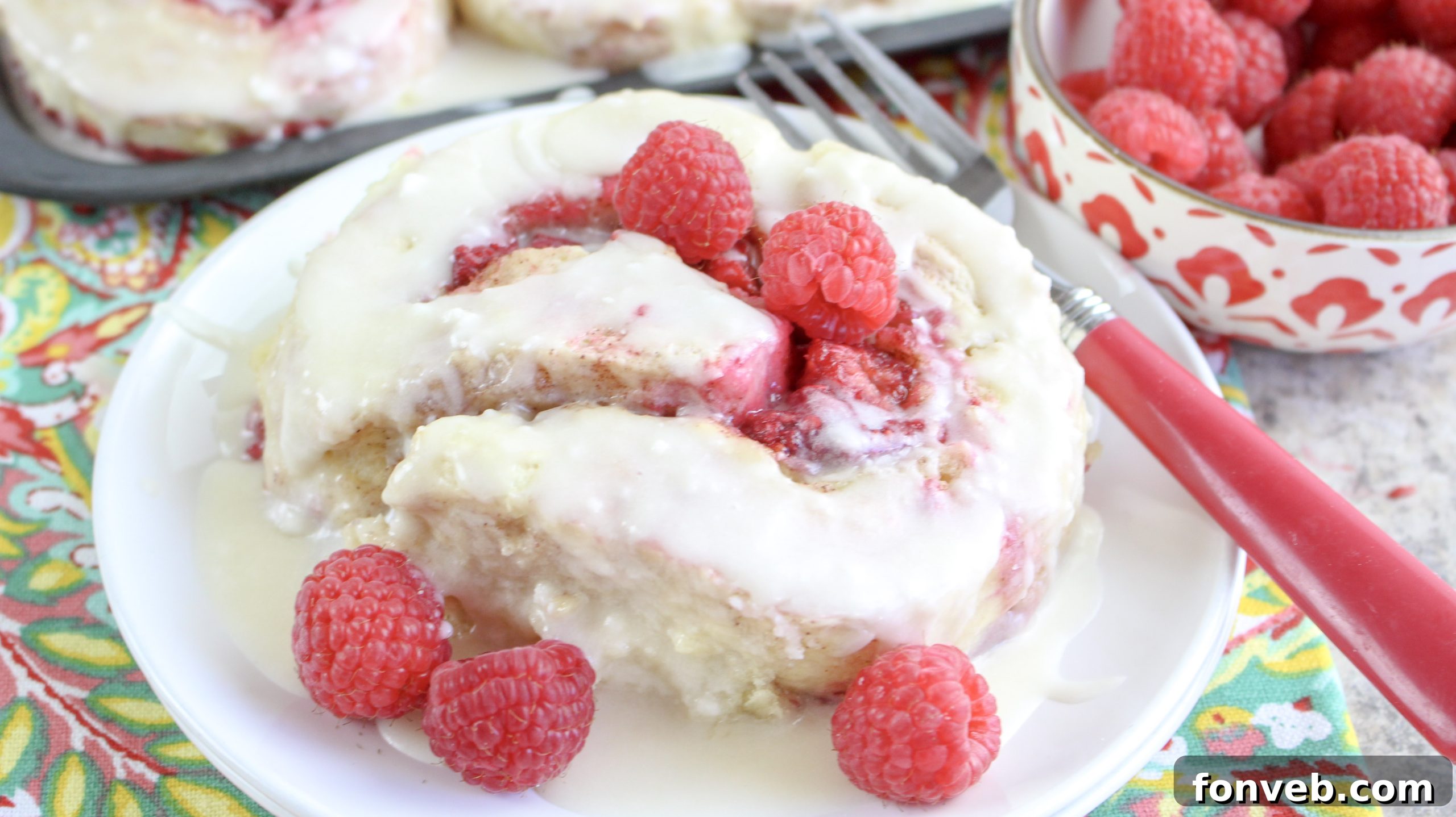 Velvet Raspberry Cinnamon Rolls 5 A hand drizzling generous amounts of creamy white icing over a tray of warm raspberry cinnamon rolls, enhancing their decadent appeal.
