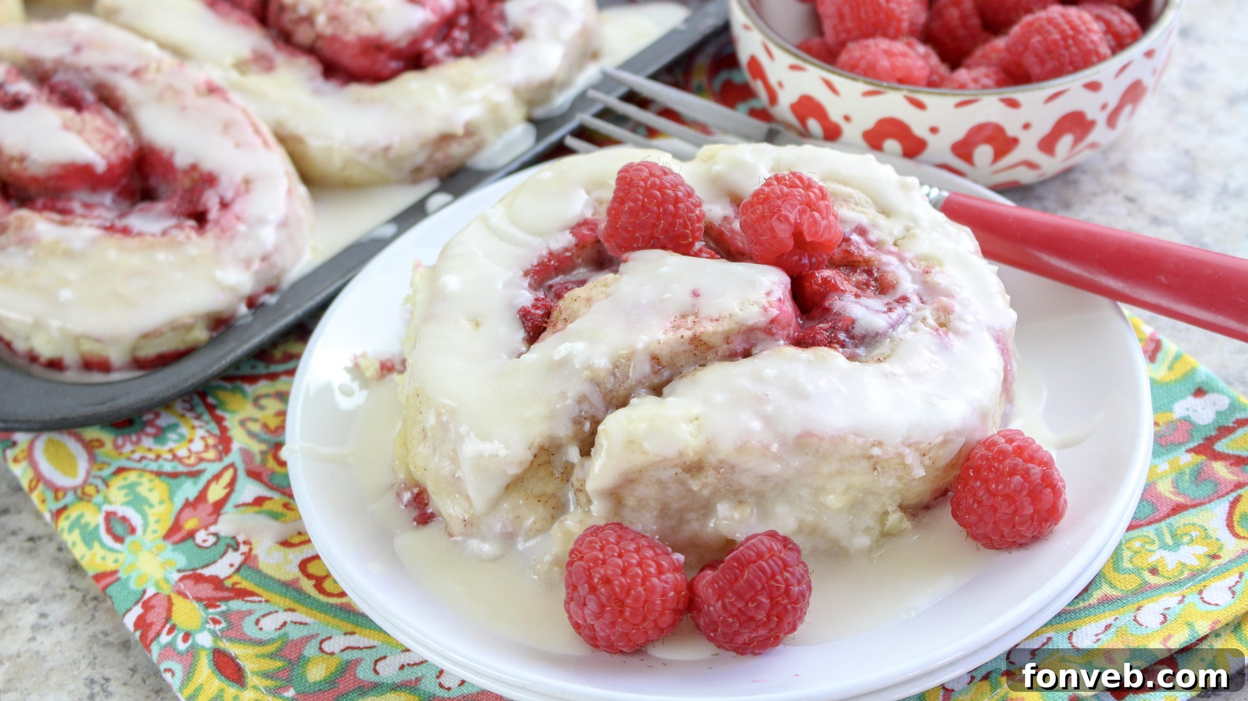 Velvet Raspberry Cinnamon Rolls 9 A display of several raspberry cinnamon rolls, perfectly baked and iced, arranged for a bake sale or a gathering.