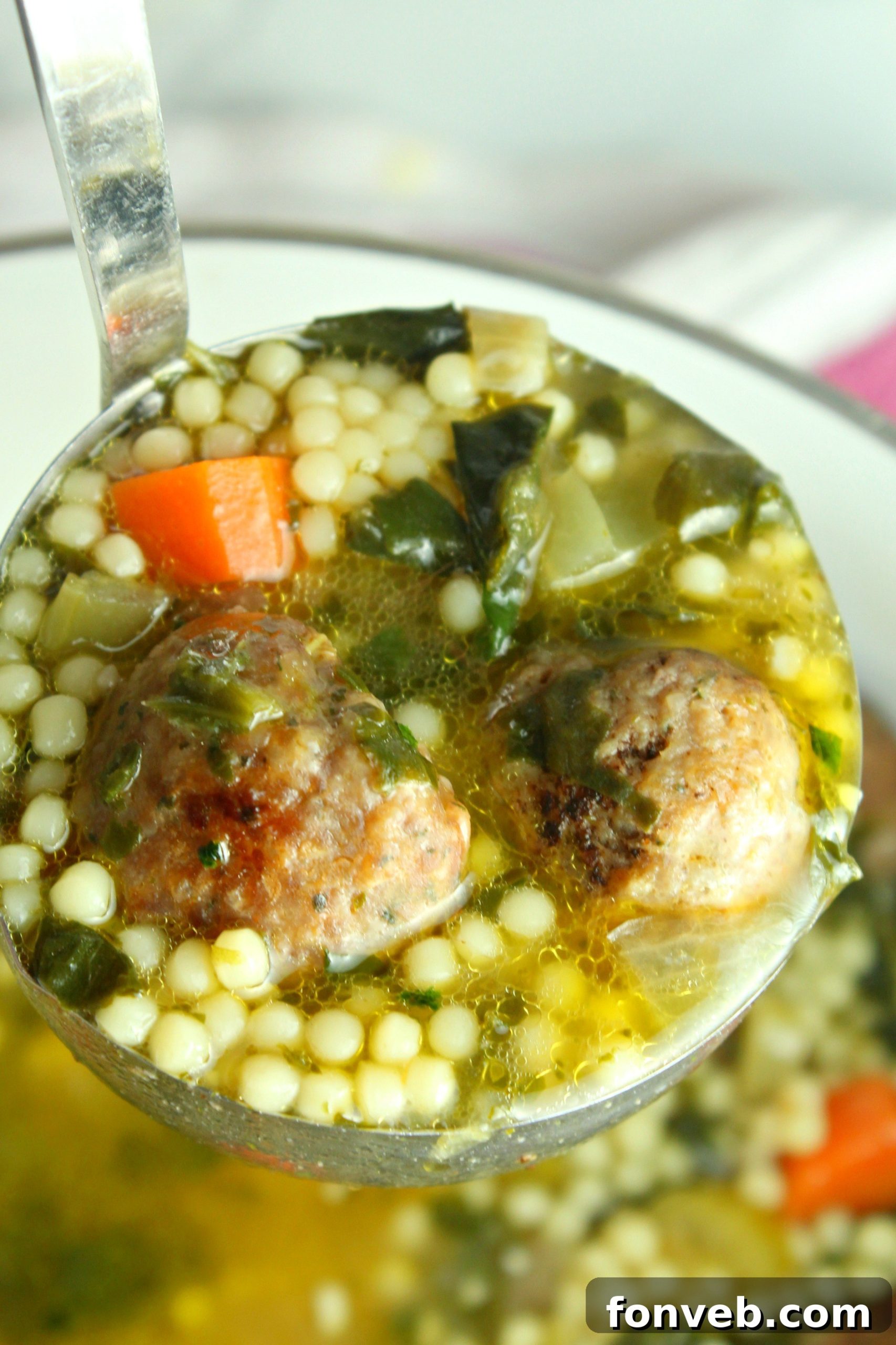 A wooden spoon filled with tiny, pearl-shaped Acini di Pepe pasta, ready to be cooked and added to a hearty soup.