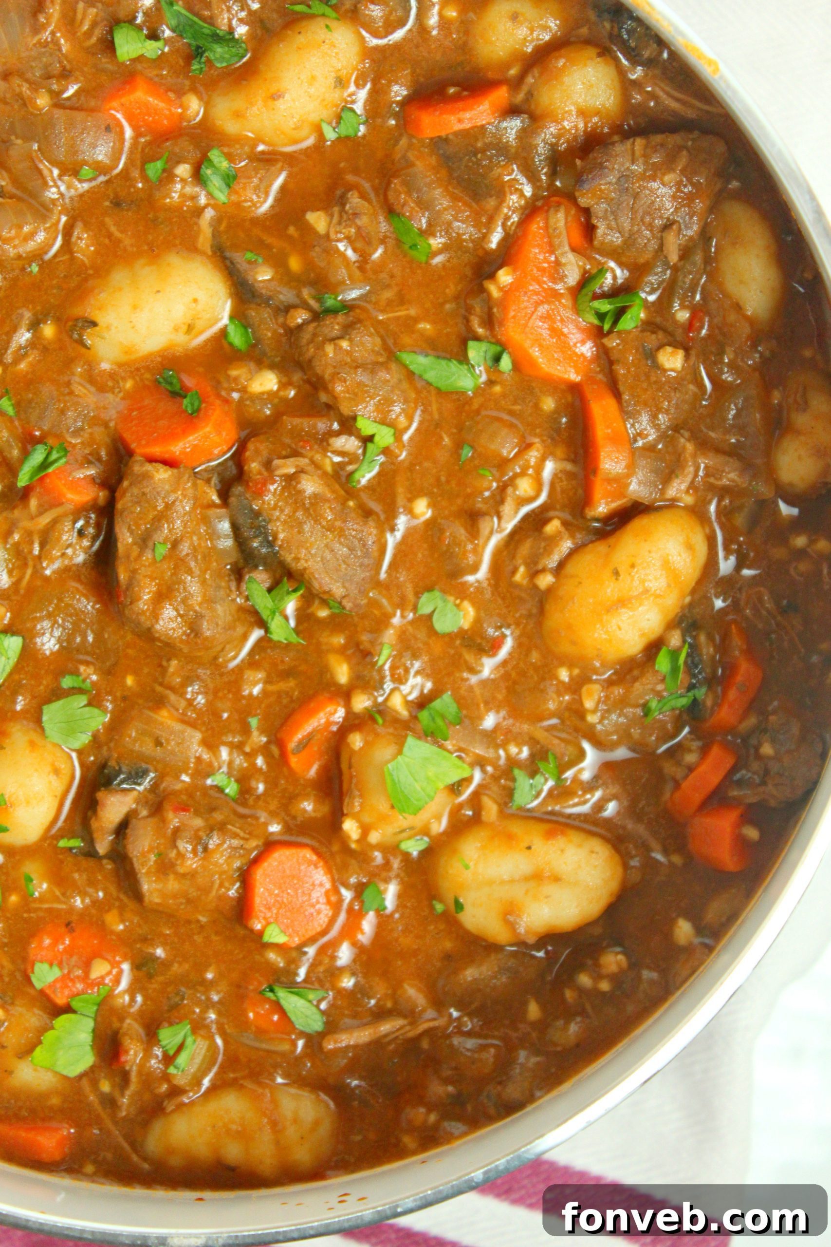 A close-up shot of a steaming bowl of chunky beef and gnocchi soup, garnished with fresh parsley.