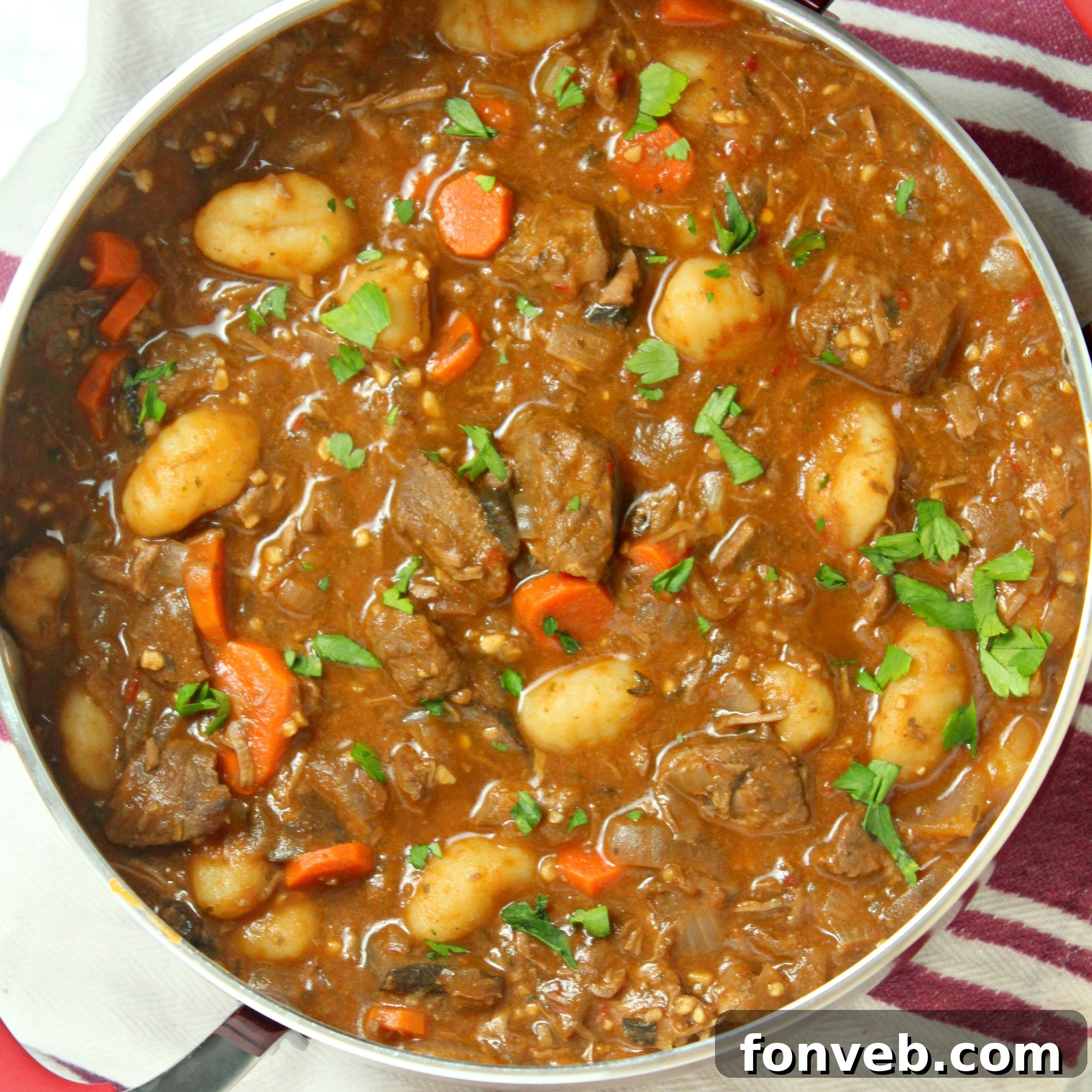 A rustic bowl of chunky beef and gnocchi soup with a spoon, highlighting the rich broth and ingredients.