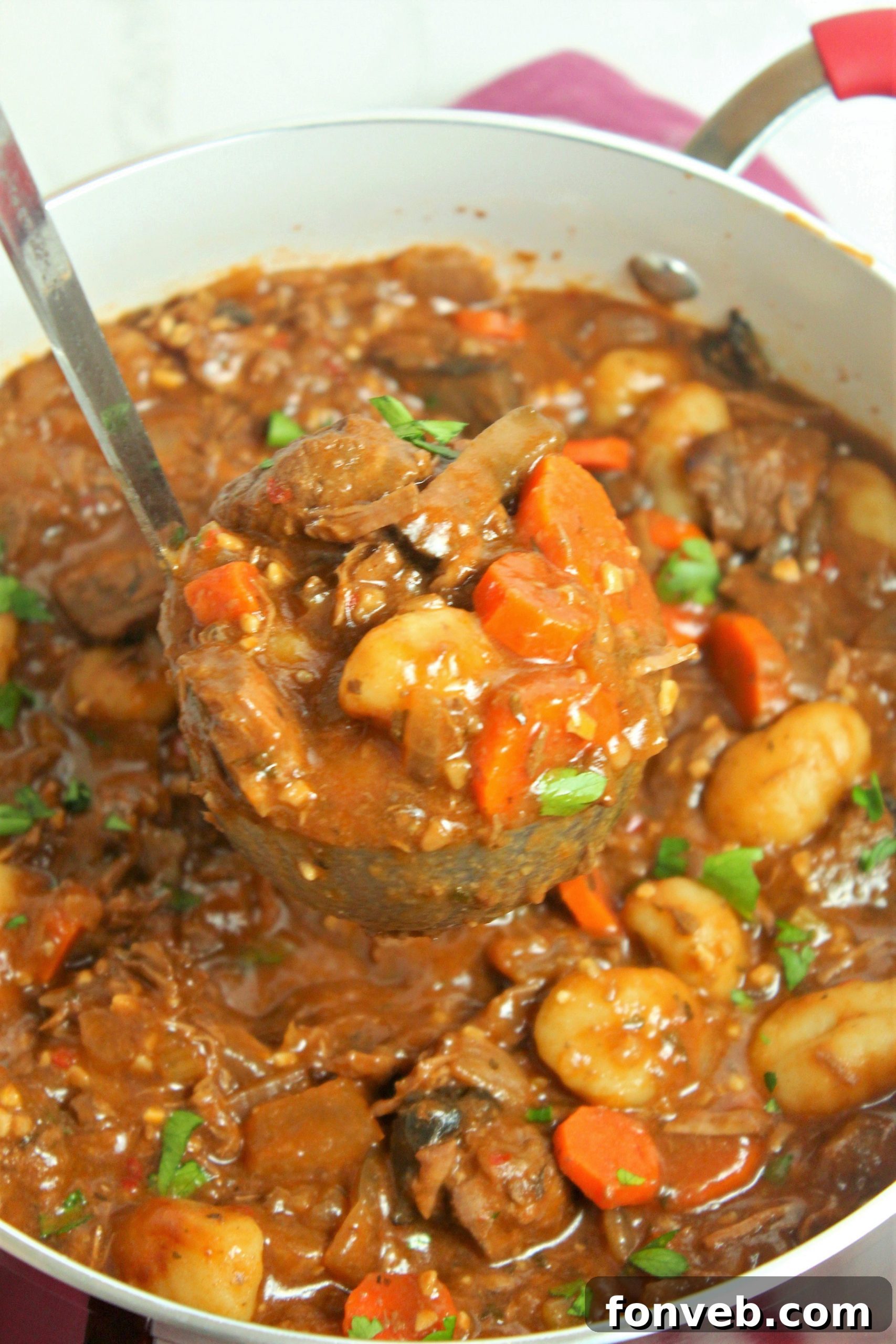 Overhead view of a pot of chunky beef and gnocchi soup simmering, showing beef pieces, vegetables, and gnocchi.