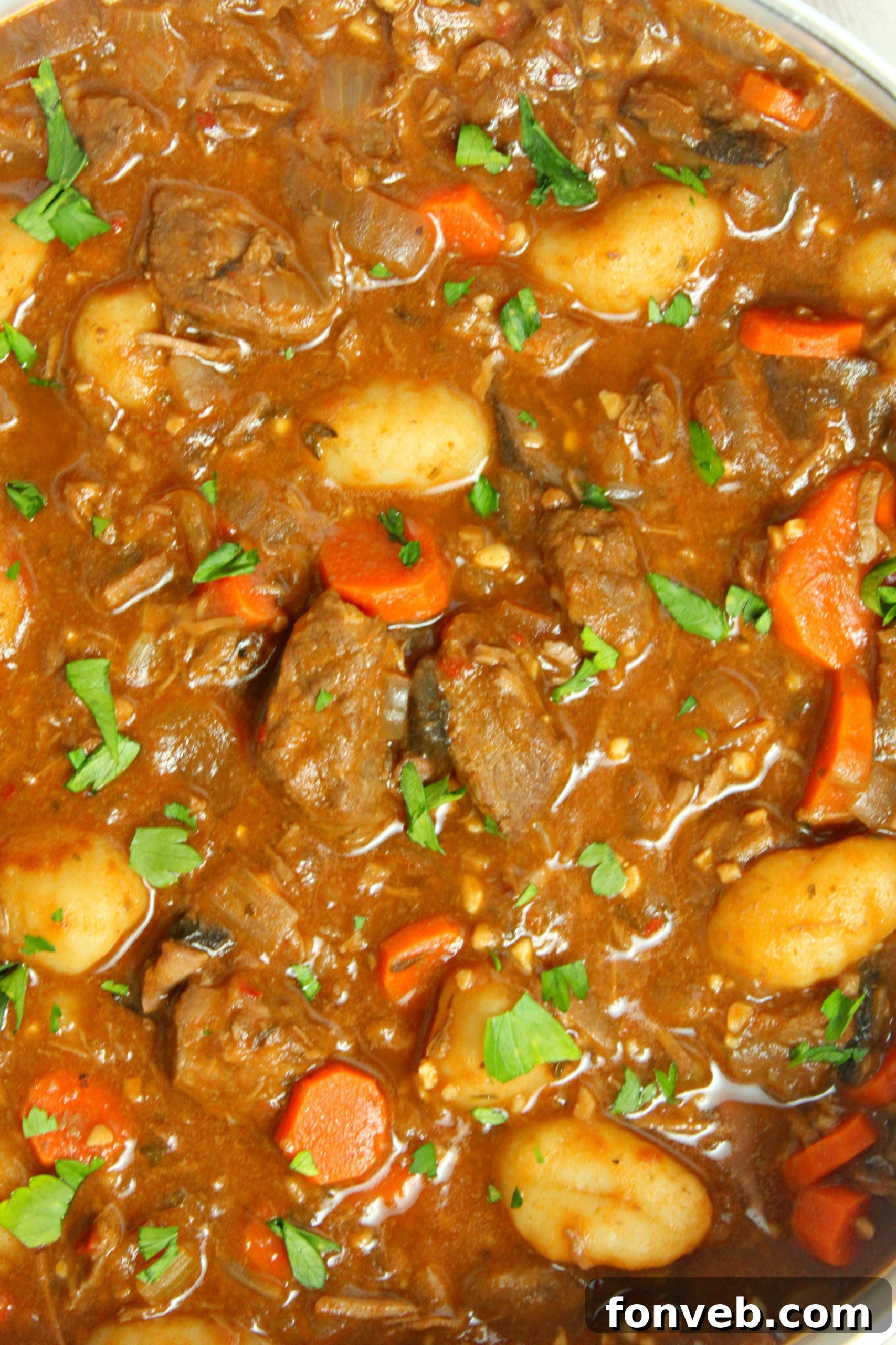 A deep bowl of chunky beef and gnocchi soup being served, steam rising from the hot meal.