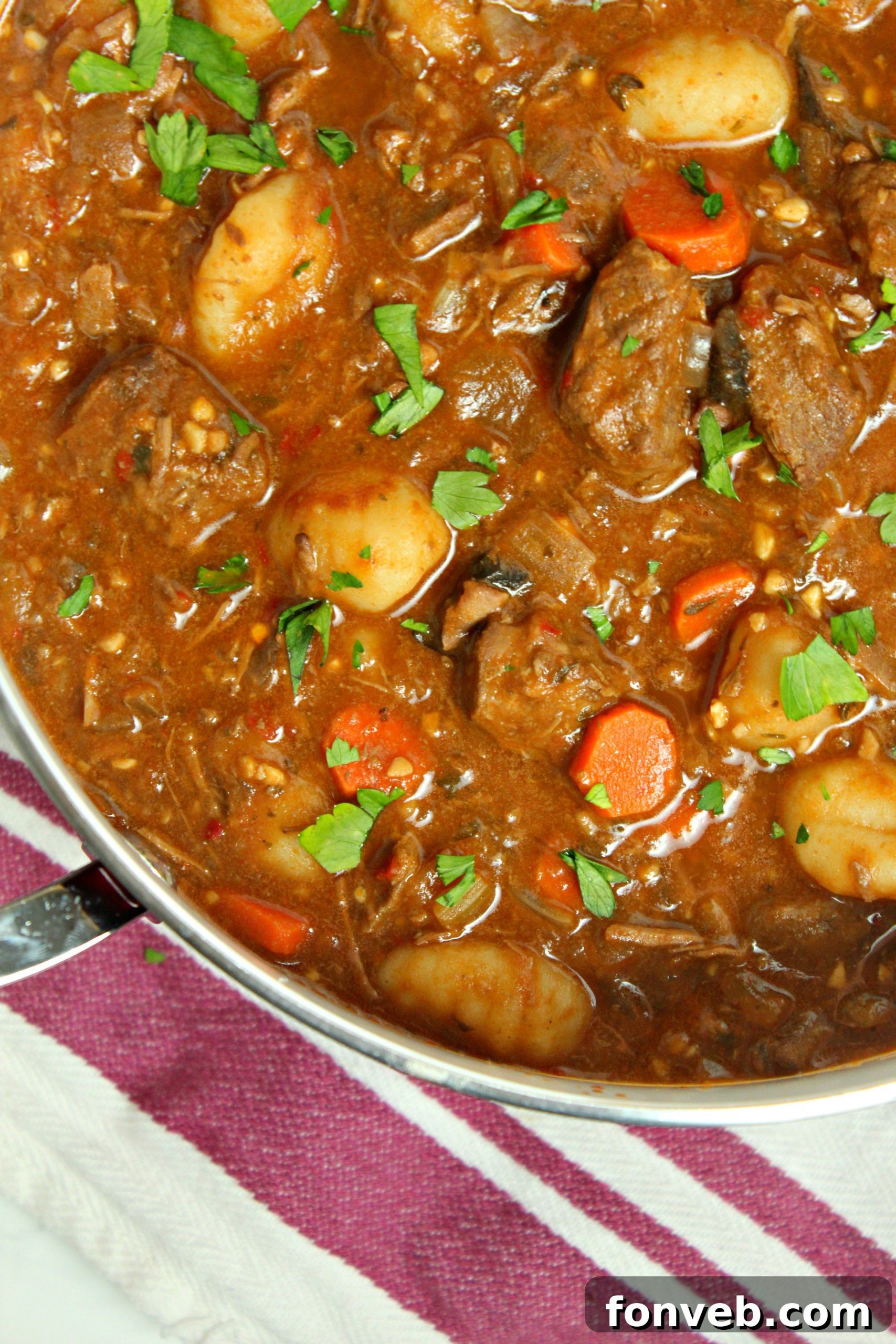 Close-up of a spoon scooping a generous portion of chunky beef and gnocchi soup, showcasing the juicy beef.
