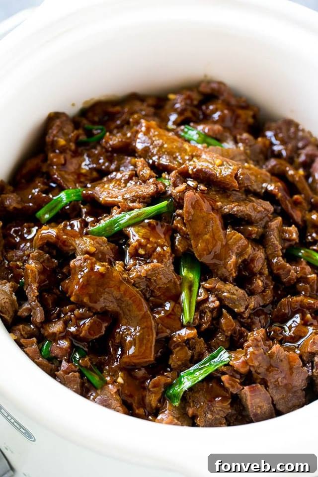 Delicious Slow Cooker Mongolian Beef, garnished with green onions and sesame seeds, served in a bowl.