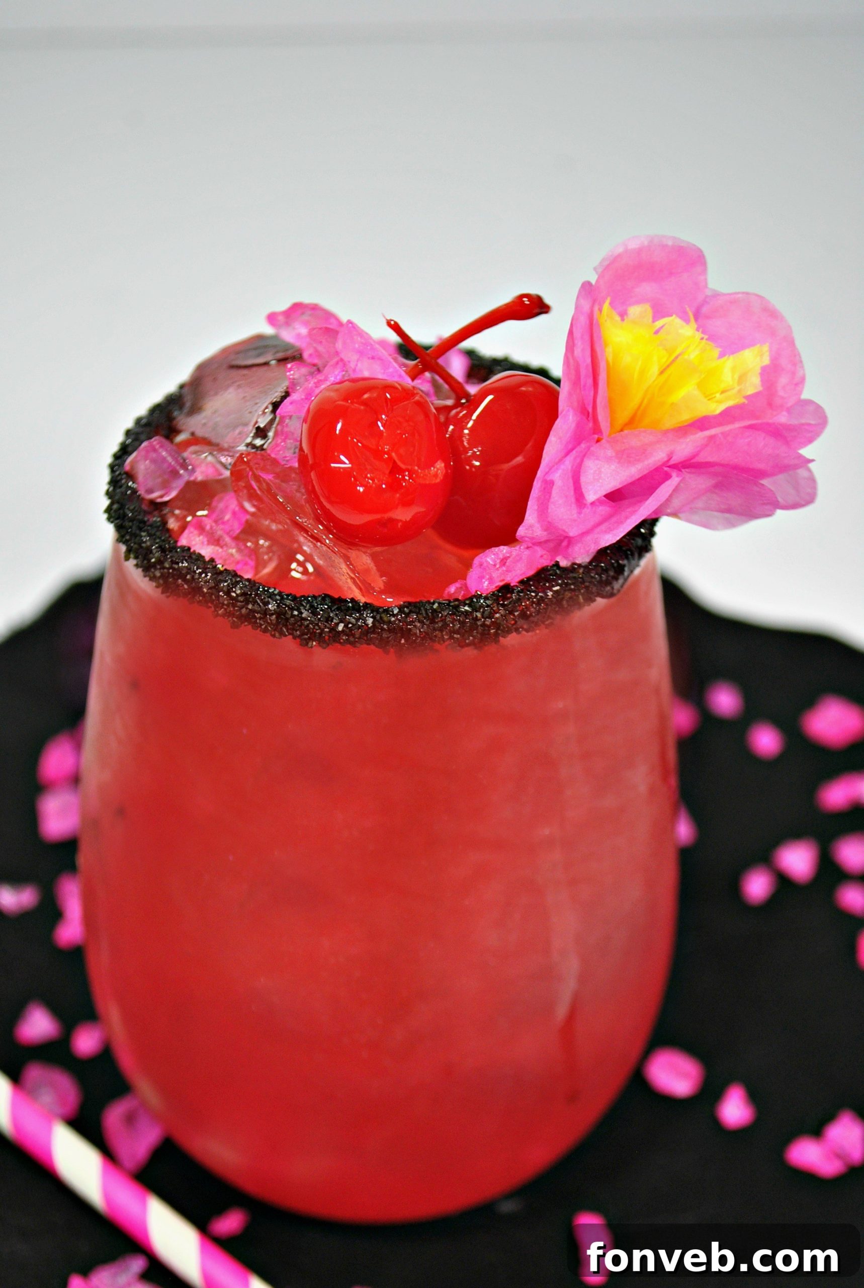 Close-up of a pink Barbie-themed cocktail in a martini glass, garnished with lime and cherries, with black sprinkles on the rim.