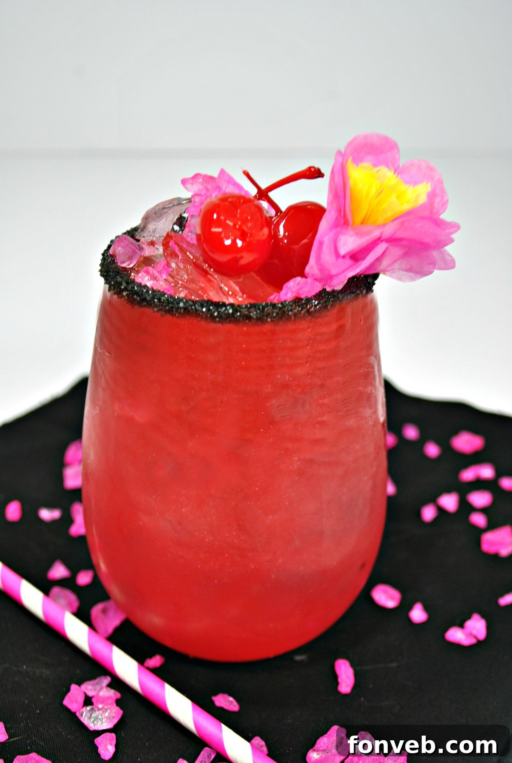 A vibrant pink Barbie cocktail, garnished with a lime wedge, a cherry, and a dark sprinkle rim, glowing against a soft background.